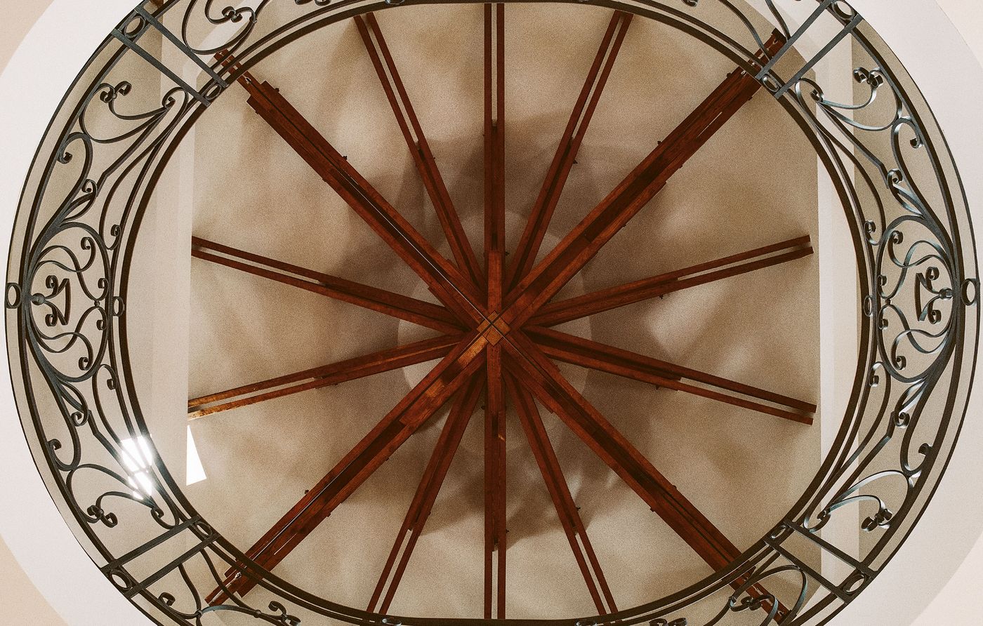 A striking overhead view of the elliptical ceiling opening, showcasing an intricate starburst pattern of wooden beams radiating from the center. This artistic ceiling detail is framed by a decorative wrought-iron railing, emphasizing the architectural artistry and grand scale of the space. A striking overhead view of the elliptical ceiling opening, showcasing an intricate starburst pattern of wooden beams radiating from the center. This artistic ceiling detail is framed by a decorative wrought-iron railing, emphasizing the architectural artistry and grand scale of the space.