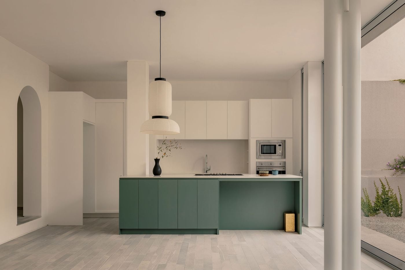 A muted green island provides the principal colour accent in Casa Tlaloc’s minimalist kitchen, contrasting with seamless white cabinetry and pale stone flooring. A sculptural paper pendant hangs overhead, while an arched doorway, slender white column and full-height glazing subtly soften the room’s strict geometry and connect it to the courtyard. A muted green island provides the principal colour accent in Casa Tlaloc’s minimalist kitchen, contrasting with seamless white cabinetry and pale stone flooring. A sculptural paper pendant hangs overhead, while an arched doorway, slender white column and full-height glazing subtly soften the room’s strict geometry and connect it to the courtyard.