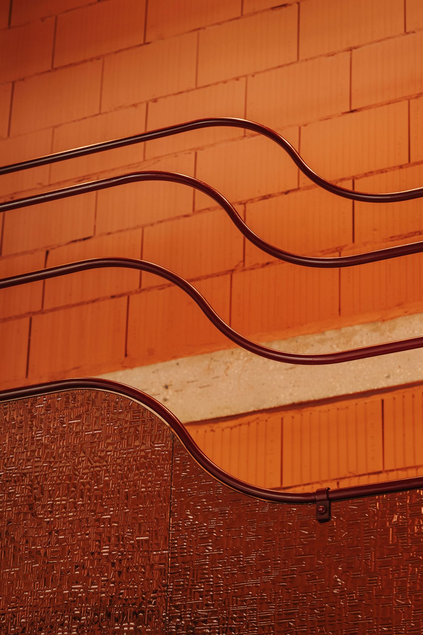 Sinuous burgundy metal railings trace gently undulating lines against terracotta-toned masonry at WIN wine bar in Warsaw. Their fluid contours evoke climbing vine tendrils, introducing an organic counterpoint to the angular industrial backdrop. Below, textured glass panels catch the warm light, adding another layer of material richness. Sinuous burgundy metal railings trace gently undulating lines against terracotta-toned masonry at WIN wine bar in Warsaw. Their fluid contours evoke climbing vine tendrils, introducing an organic counterpoint to the angular industrial backdrop. Below, textured glass panels catch the warm light, adding another layer of material richness.