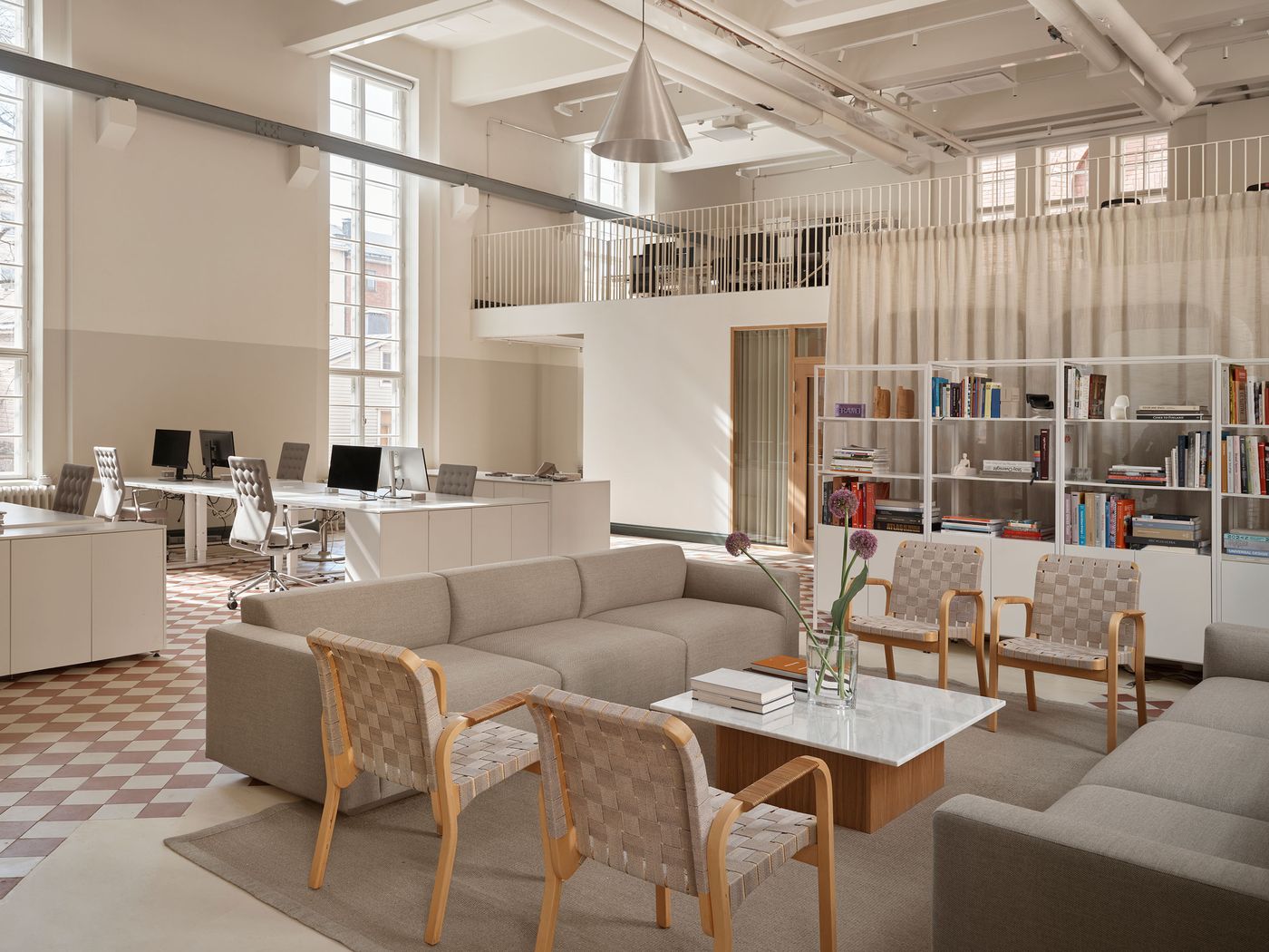A versatile office and lounge space features modular seating and modern workstations on a patterned red and white floor. Overhead, exposed industrial pipes and sleek lighting enhance the raw aesthetic, balanced by the minimalist Scandinavian furniture and design library. A versatile office and lounge space features modular seating and modern workstations on a patterned red and white floor. Overhead, exposed industrial pipes and sleek lighting enhance the raw aesthetic, balanced by the minimalist Scandinavian furniture and design library.