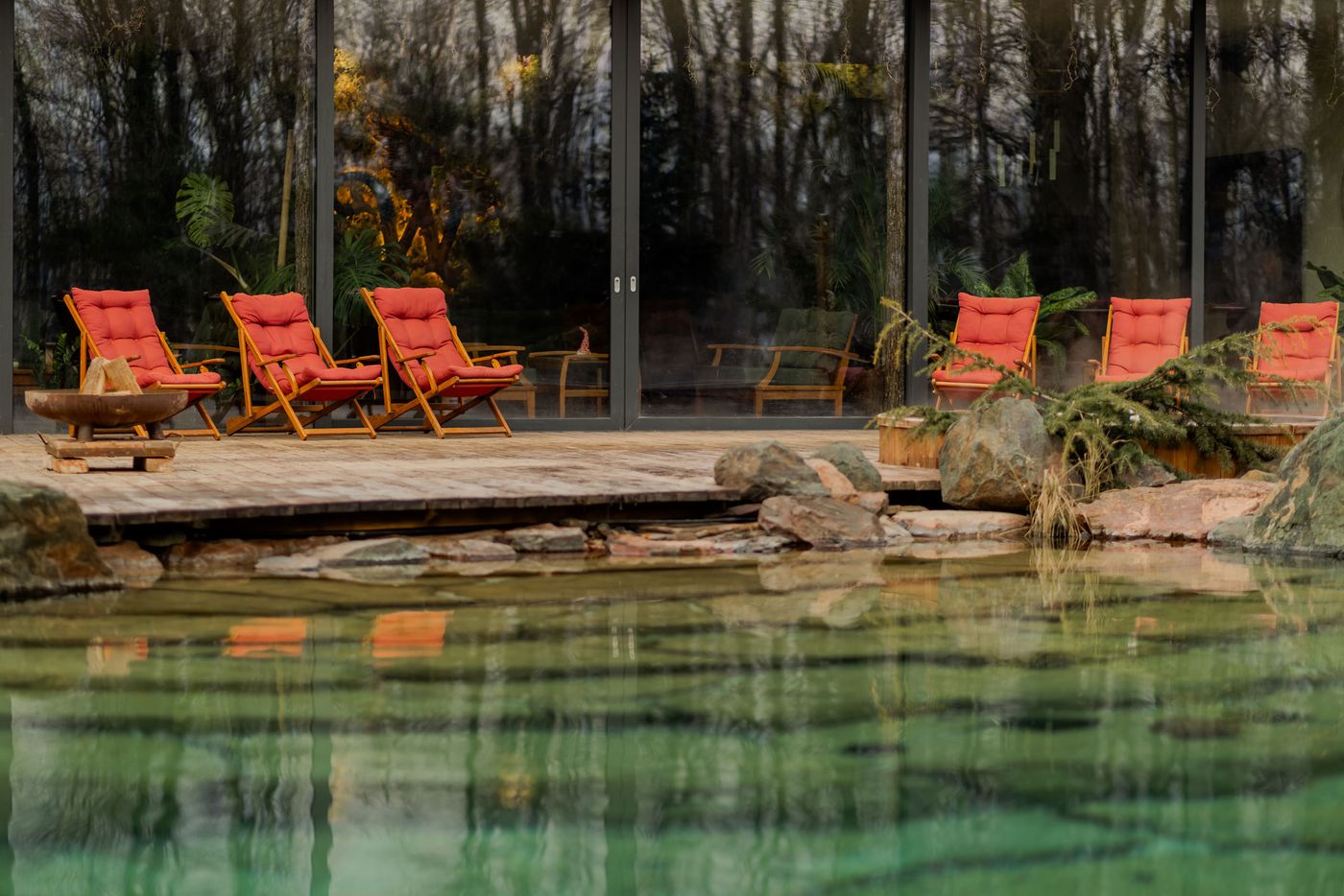 A serene lakeside scene featuring red cushioned lounge chairs on a wooden deck, surrounded by greenery and a reflective water surface. A serene lakeside scene featuring red cushioned lounge chairs on a wooden deck, surrounded by greenery and a reflective water surface.