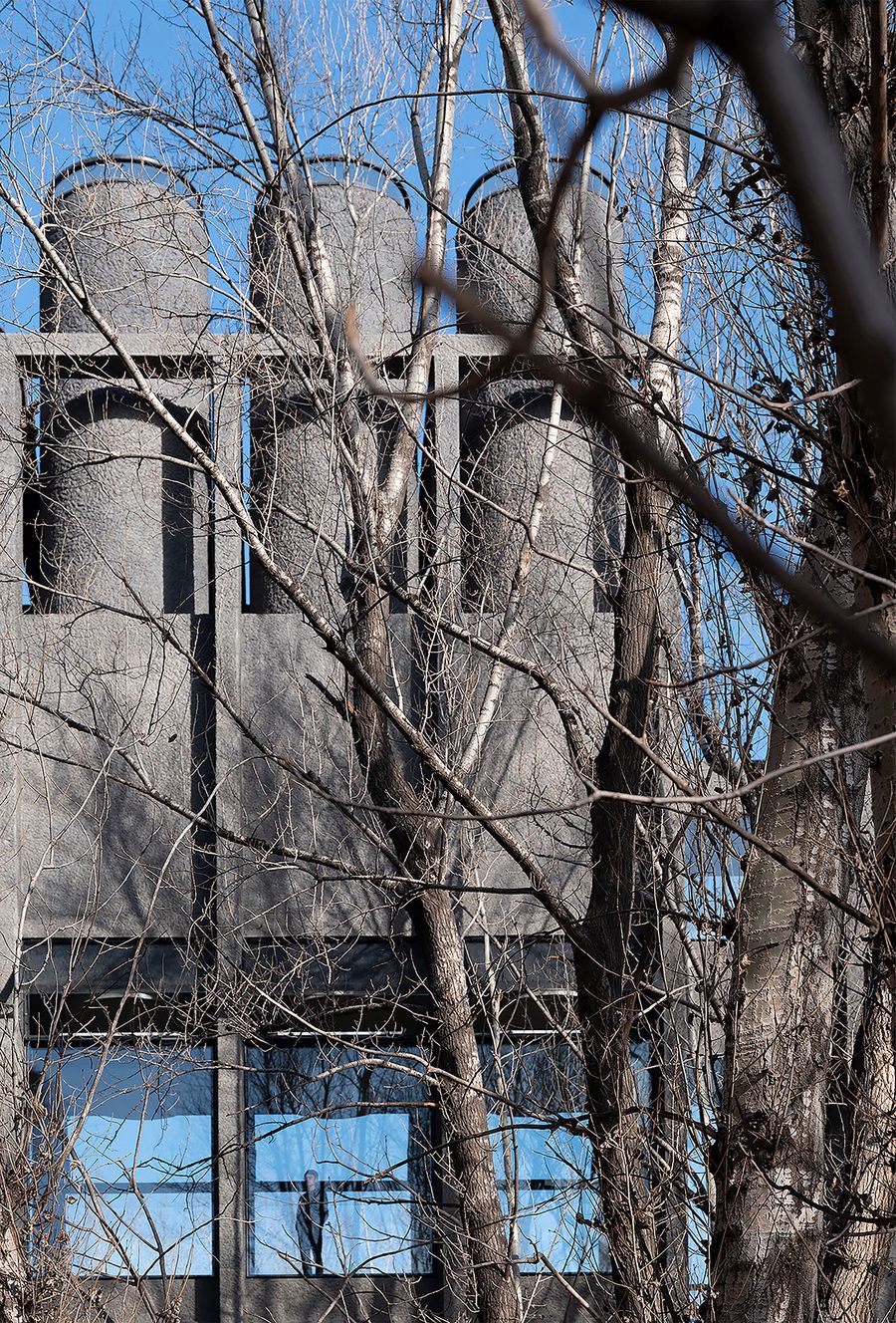 A modern industrial building with three cylindrical structures peeks through bare trees against a clear blue sky. A modern industrial building with three cylindrical structures peeks through bare trees against a clear blue sky.