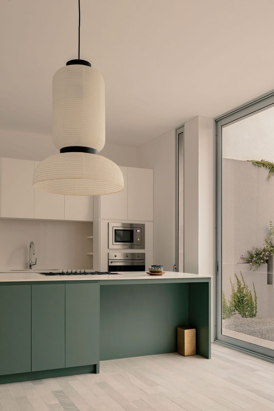 Casa Tlaloc’s kitchen is defined by crisp white cabinetry and a muted green island that provides the room’s strongest colour accent. A large paper pendant introduces softness overhead, while floor-to-ceiling glazing opens directly towards the planted courtyard, reinforcing the house’s close relationship between interior and garden. Casa Tlaloc’s kitchen is defined by crisp white cabinetry and a muted green island that provides the room’s strongest colour accent. A large paper pendant introduces softness overhead, while floor-to-ceiling glazing opens directly towards the planted courtyard, reinforcing the house’s close relationship between interior and garden.
