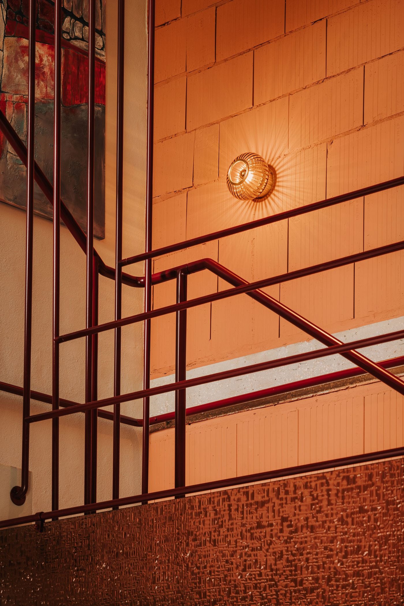 A close-up of WIN's custom wine shelving reveals an intricate framework of slender burgundy metal rods, with individual compartments accommodating champagne bottles both upright and horizontally. The precise geometry of the structure contrasts with the rough concrete wall behind it and the pale, subtly speckled flooring below. A close-up of WIN's custom wine shelving reveals an intricate framework of slender burgundy metal rods, with individual compartments accommodating champagne bottles both upright and horizontally. The precise geometry of the structure contrasts with the rough concrete wall behind it and the pale, subtly speckled flooring below.