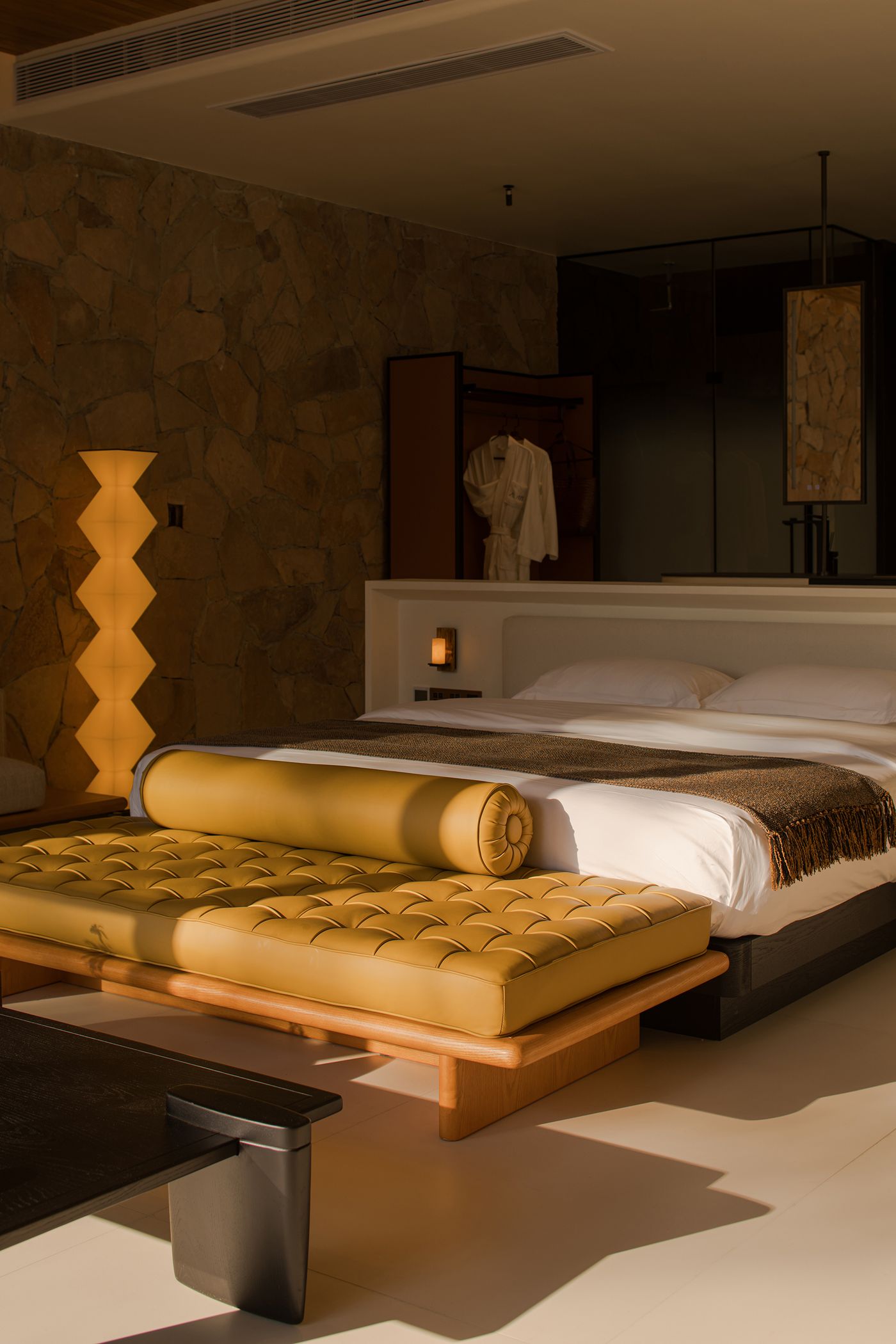 Stylishly designed hotel room featuring a yellow bed with a bolster, stone wall, and elegant lighting for a cozy ambiance. Stylishly designed hotel room featuring a yellow bed with a bolster, stone wall, and elegant lighting for a cozy ambiance.