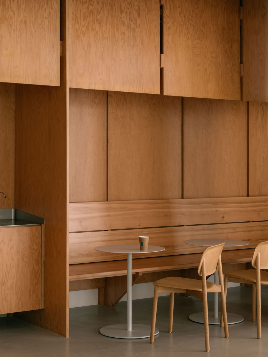A quiet vignette of the café features light oak built-ins and simple circular tables, evoking a Japanese-Scandinavian sensibility rooted in tactility and material honesty.