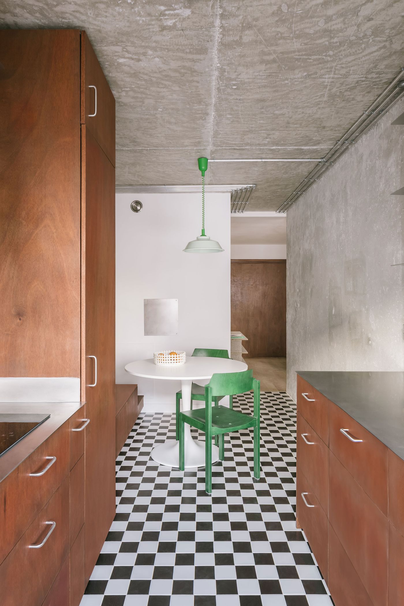 Modern kitchen with wood cabinets, black and white checkered floor, round table, and green chairs under a green pendant light. Modern kitchen with wood cabinets, black and white checkered floor, round table, and green chairs under a green pendant light.