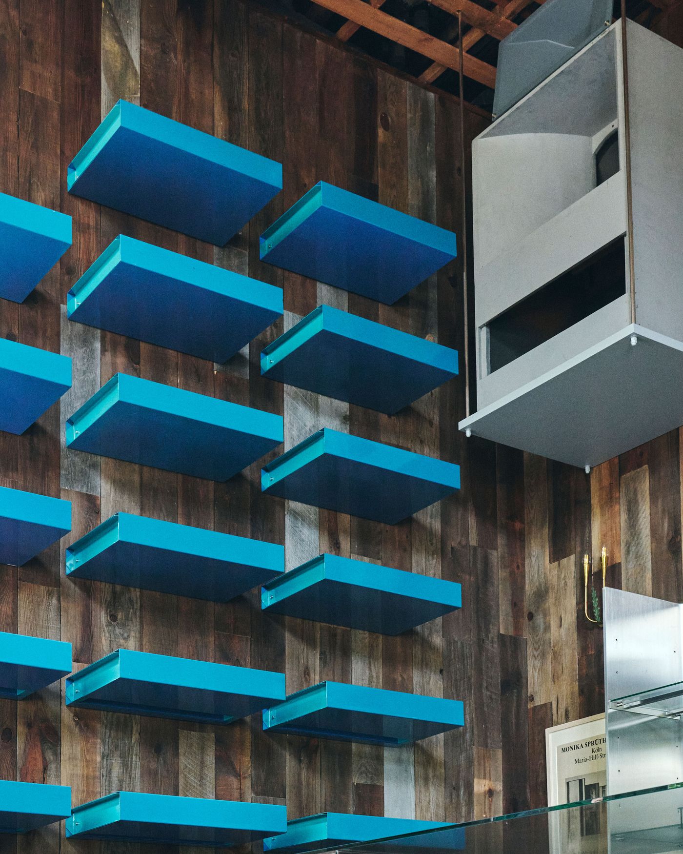 A wall with vibrant blue shelves arranged in a grid pattern, contrasting against a rustic wooden background.