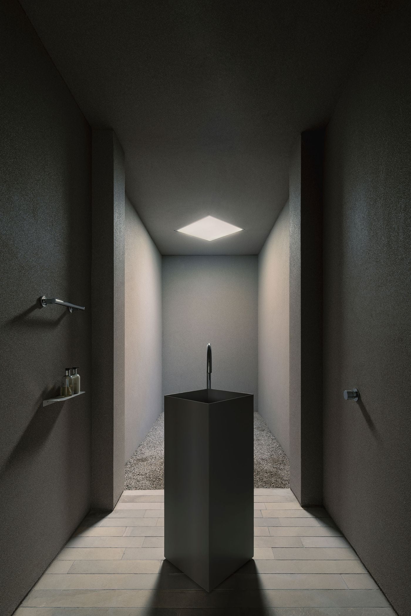 Casa Tlaloc’s guest WC takes on an almost monastic character, enclosed by dark grey surfaces and lit primarily through a square skylight. A freestanding black metal basin rises from the centre of the narrow space, aligned with a gravel-filled recess beyond to create an unexpectedly contemplative setting for an everyday ritual. Casa Tlaloc’s guest WC takes on an almost monastic character, enclosed by dark grey surfaces and lit primarily through a square skylight. A freestanding black metal basin rises from the centre of the narrow space, aligned with a gravel-filled recess beyond to create an unexpectedly contemplative setting for an everyday ritual.