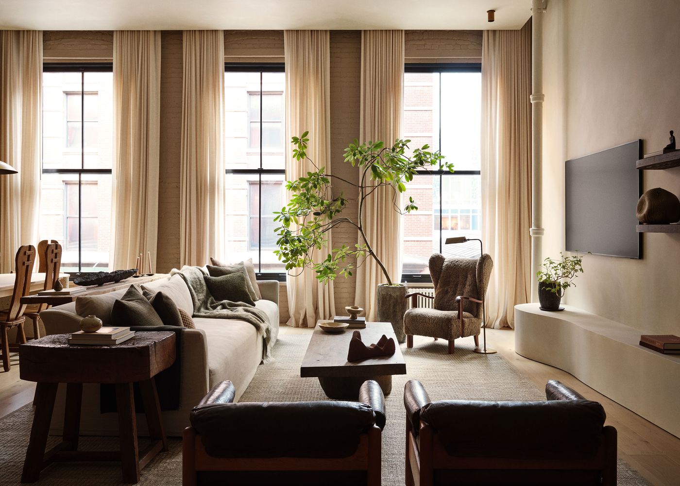 A cozy modern living room with large windows, a plush sofa with throw pillows, wooden furniture, and decorative plants. A cozy modern living room with large windows, a plush sofa with throw pillows, wooden furniture, and decorative plants.