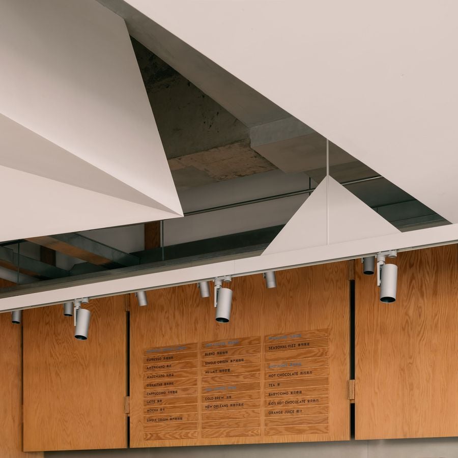 A detail view of the ceiling reveals a triangular cutout framing the raw concrete above, juxtaposing the precision of white plaster surfaces with the roughness of exposed structure.