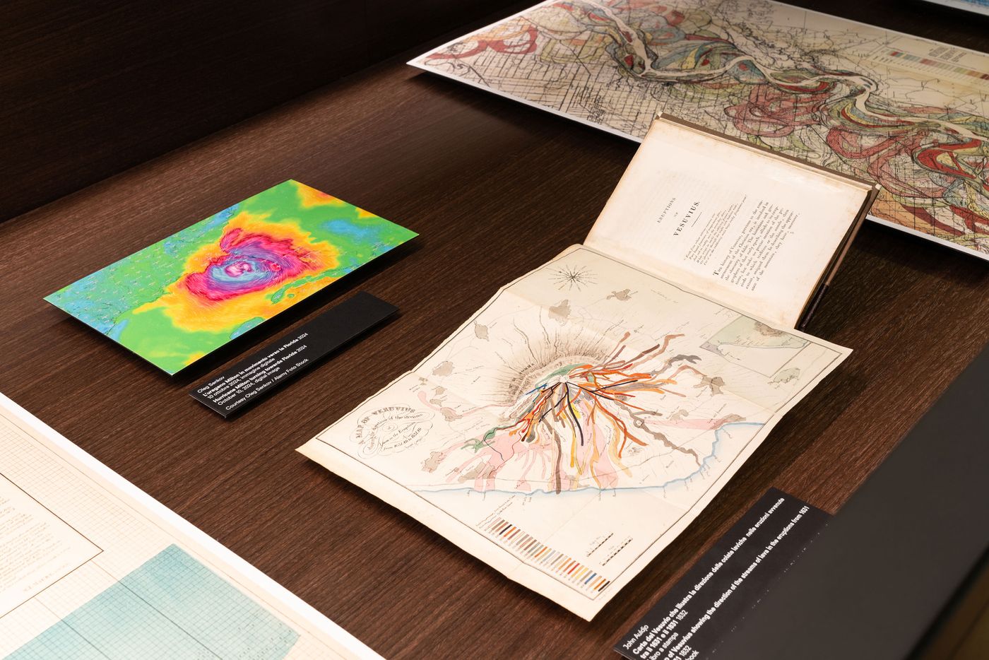 A colorful topographic map beside an antique volcanic eruption map, displayed on a wooden surface, showcasing geological studies. A colorful topographic map beside an antique volcanic eruption map, displayed on a wooden surface, showcasing geological studies.