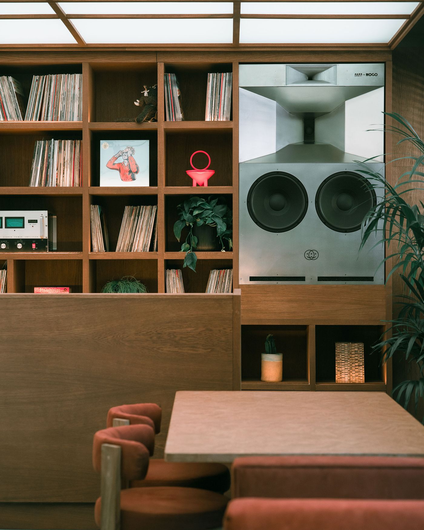 A cozy room featuring a large speaker system, vinyl records, and retro decor, complemented by wooden shelves and a stylish dining table.