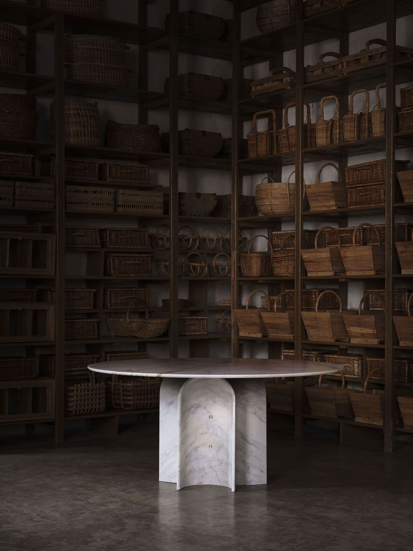 Minimalist marble table with a sculptural curved base, set against a backdrop of rustic wooden shelves filled with woven baskets. Minimalist marble table with a sculptural curved base, set against a backdrop of rustic wooden shelves filled with woven baskets.