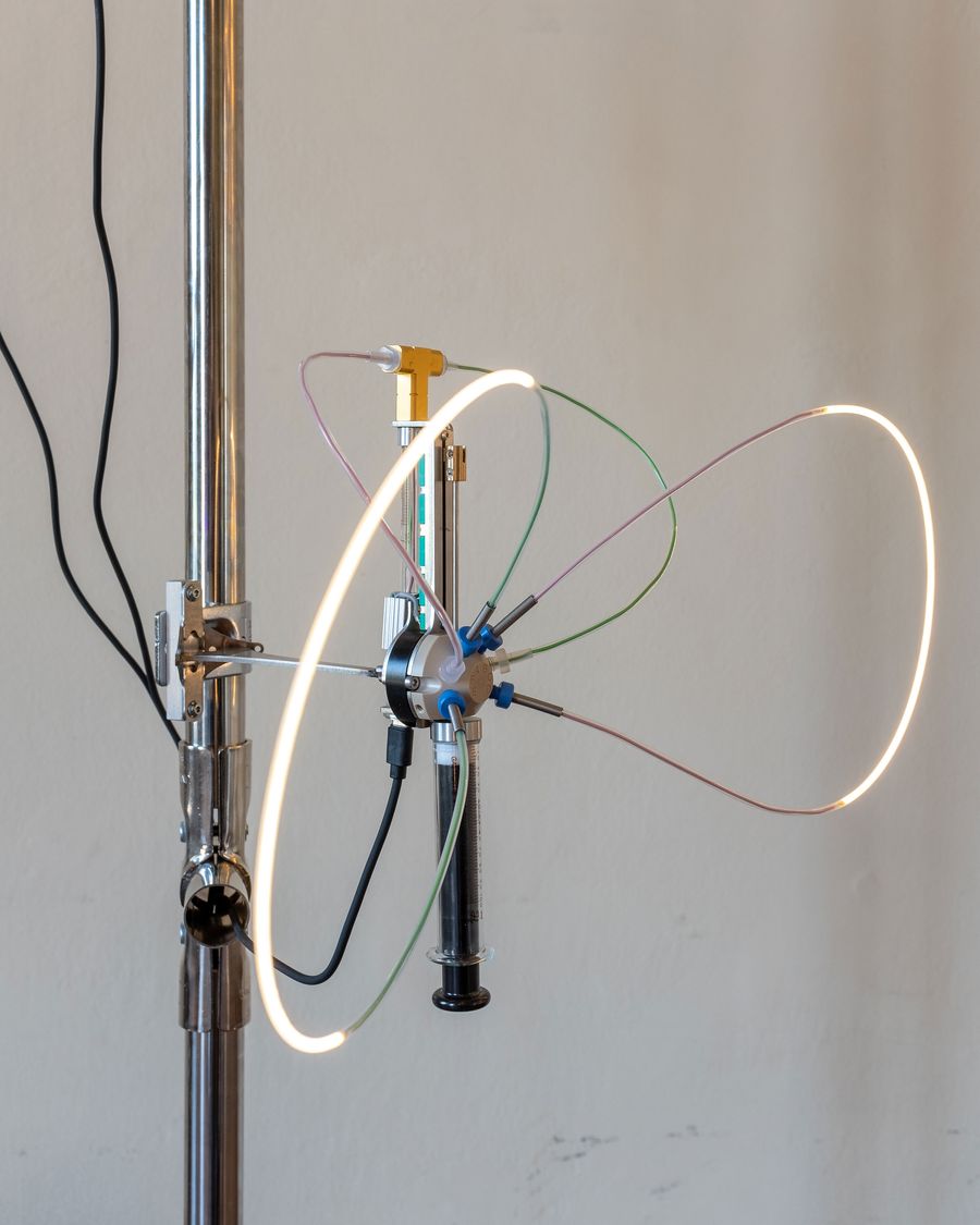 Close-up of a mechanical light structure featuring a central hub with radiating LED-tipped wires and translucent tubing, mounted on a chrome vertical support—precision meets softness in form. Close-up of a mechanical light structure featuring a central hub with radiating LED-tipped wires and translucent tubing, mounted on a chrome vertical support—precision meets softness in form.