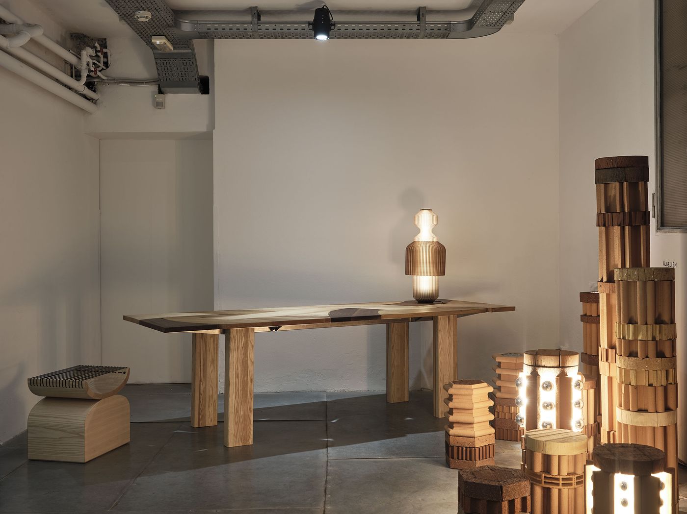 Sculptural wooden table with faceted lamp and stacked terracotta lighting forms in a minimalist, industrial interior.