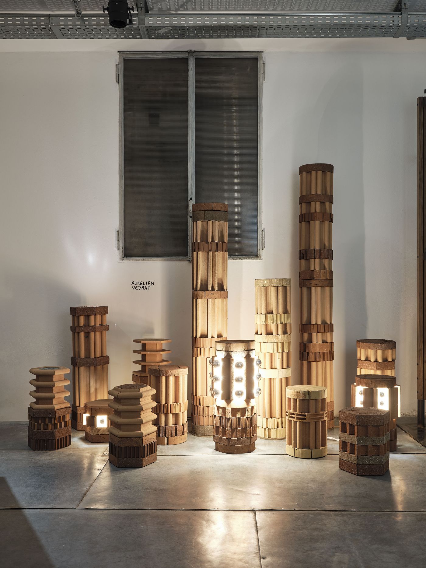 A group of cylindrical terracotta light sculptures arranged like a glowing urban skyline in a dimly lit room.
