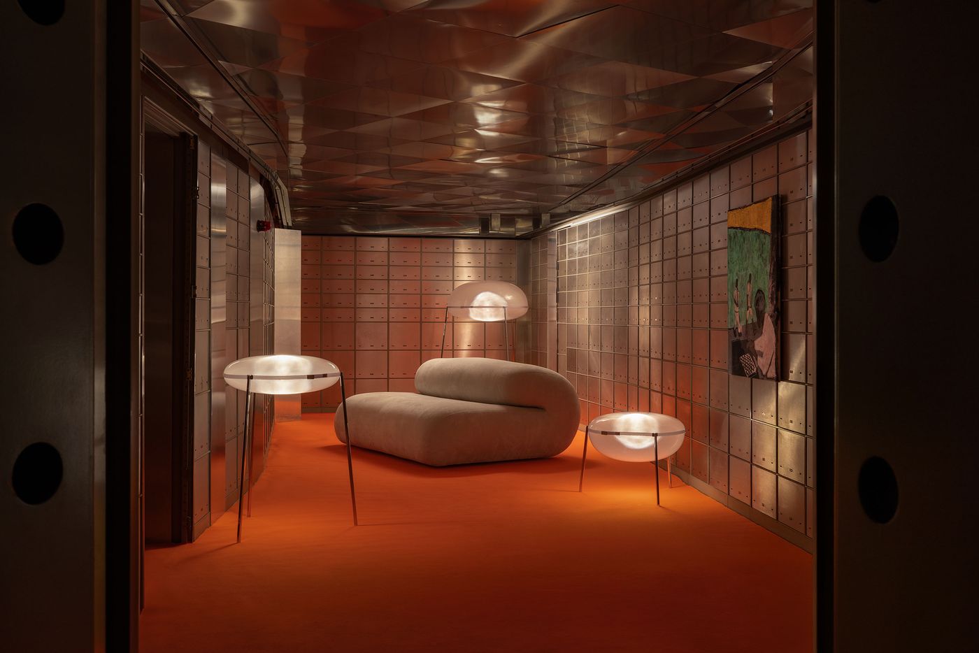 A futuristic lounge with an orange carpet, metallic safety deposit box walls, and glowing frosted glass lights that resemble space-age mushrooms.