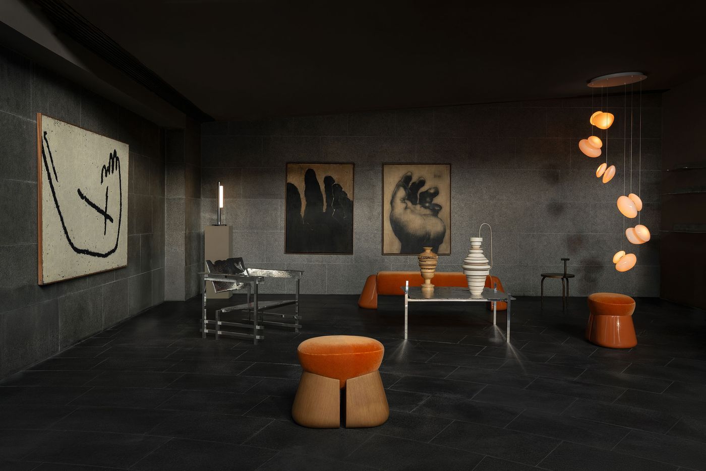 An atmospheric interior with a curated selection of modern furniture and lighting in warm tones, set against dark stone walls adorned with abstract and figurative artworks.