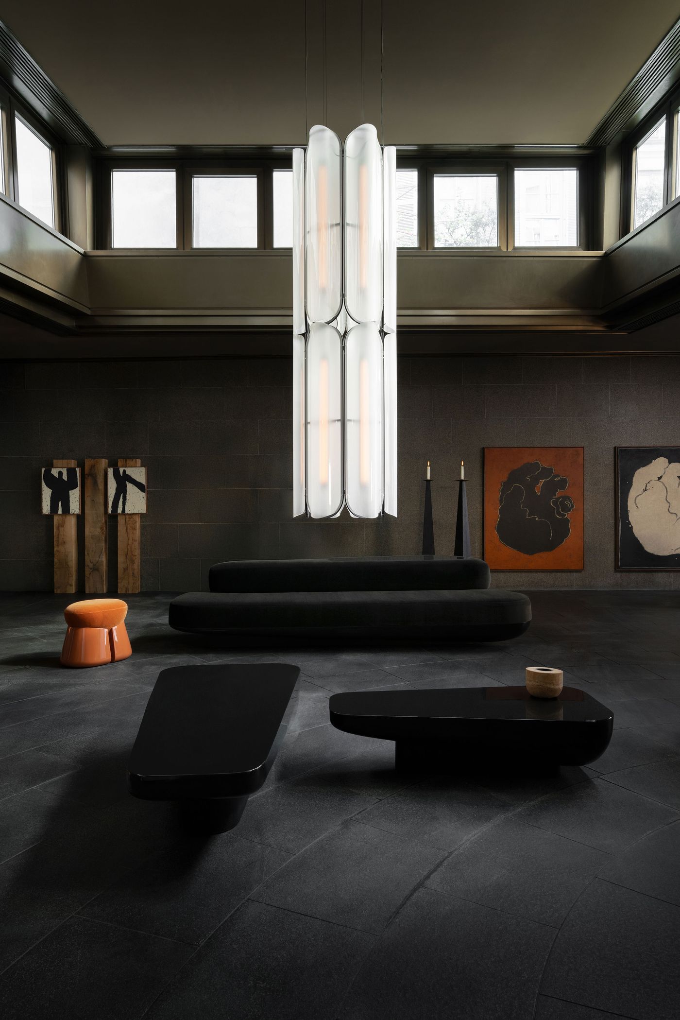 A grand, double-height space featuring a striking vertical chandelier of curved white glass panels, contrasted by dark furniture and floor tiles.