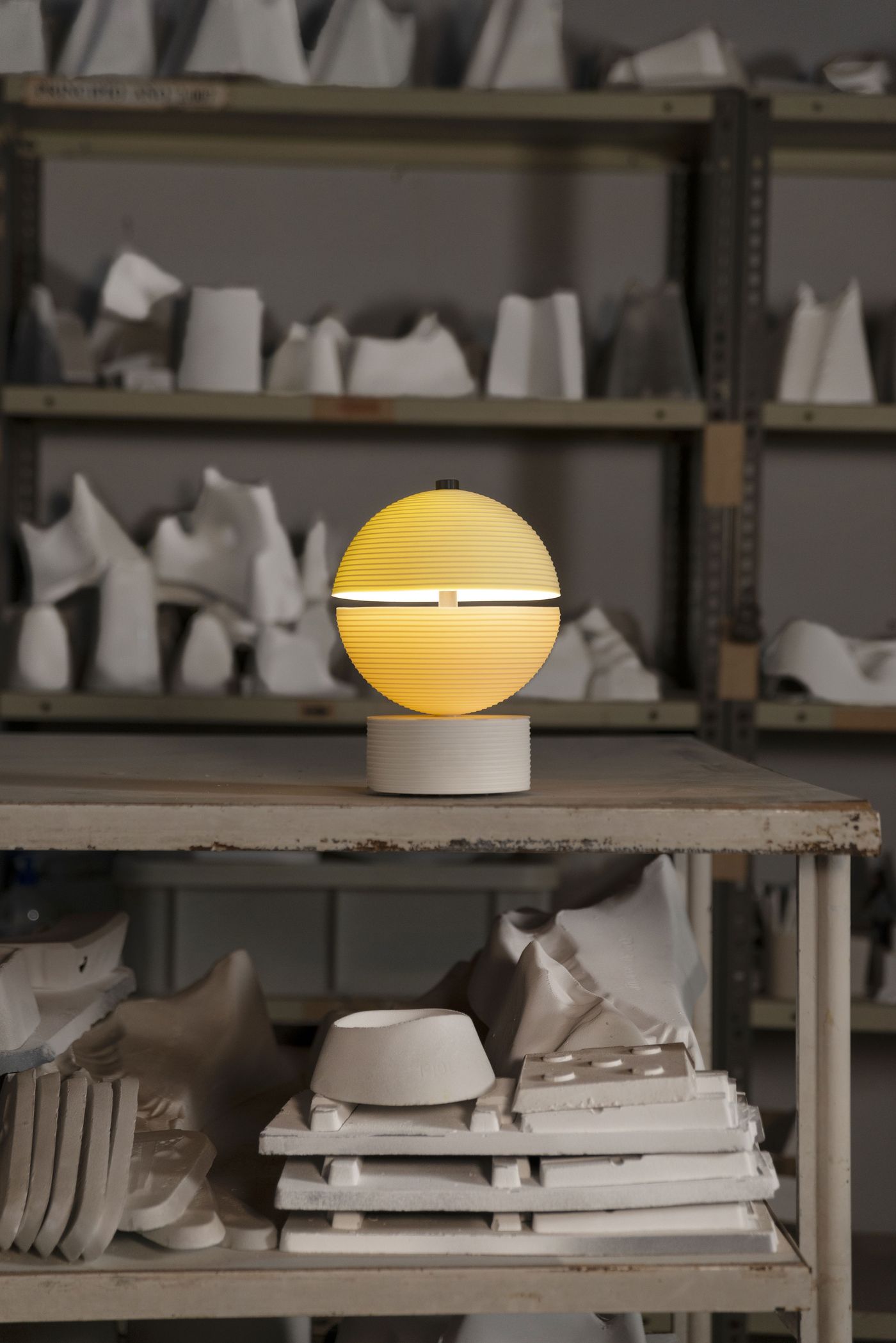 A glowing ribbed sphere sits atop a ridged cylindrical base, casting a warm ambient light in a ceramics studio filled with white plaster molds—Lee Broom’s poetic design for Lladró blurs the line between craft and sculpture. A glowing ribbed sphere sits atop a ridged cylindrical base, casting a warm ambient light in a ceramics studio filled with white plaster molds—Lee Broom’s poetic design for Lladró blurs the line between craft and sculpture.
