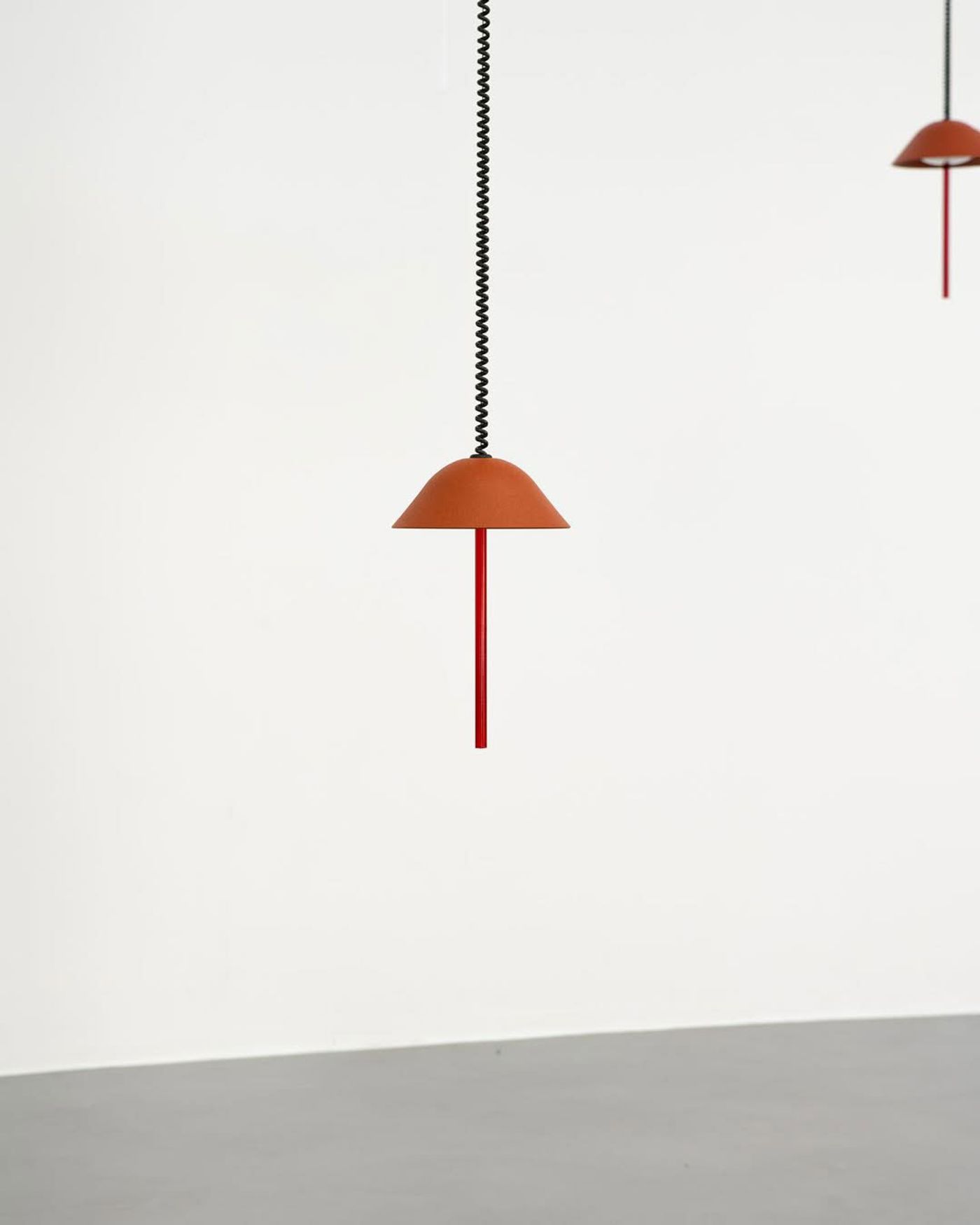 A close-up of a terracotta-colored pendant light with a red rod, suspended from a black twisted cord.