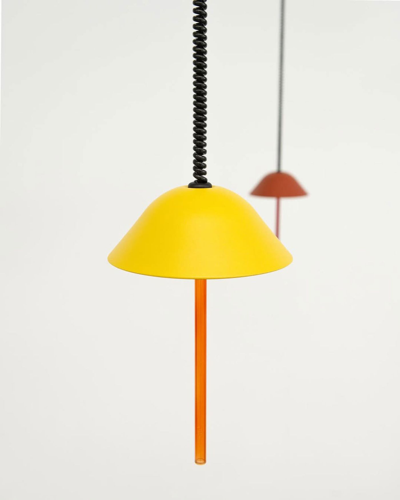 A bright yellow pendant light with an orange rod, glowing against a clean white background.