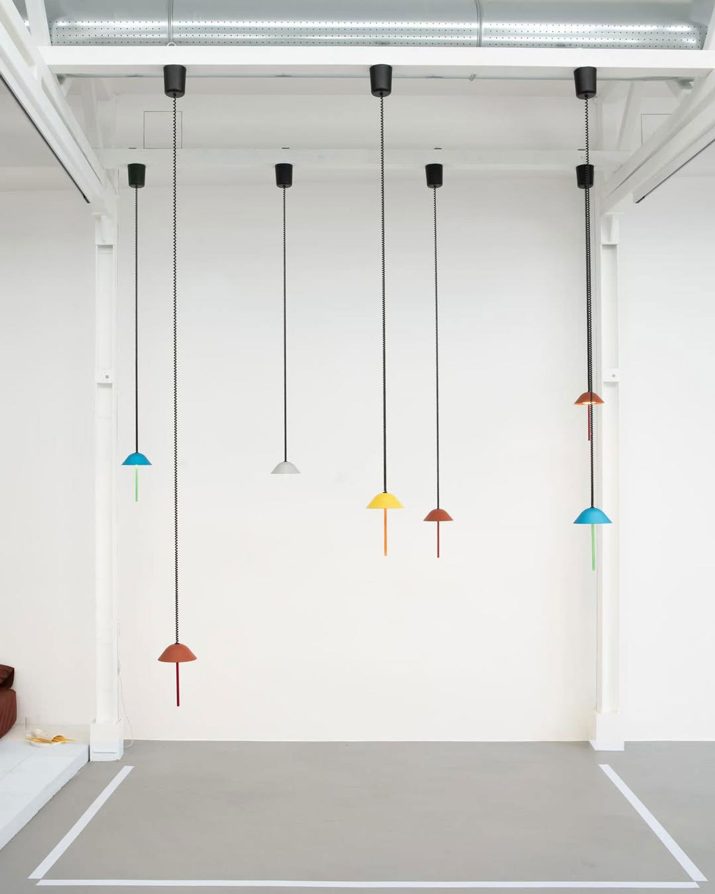 A cluster of colorful, minimalist pendant lights hanging from a white industrial ceiling.