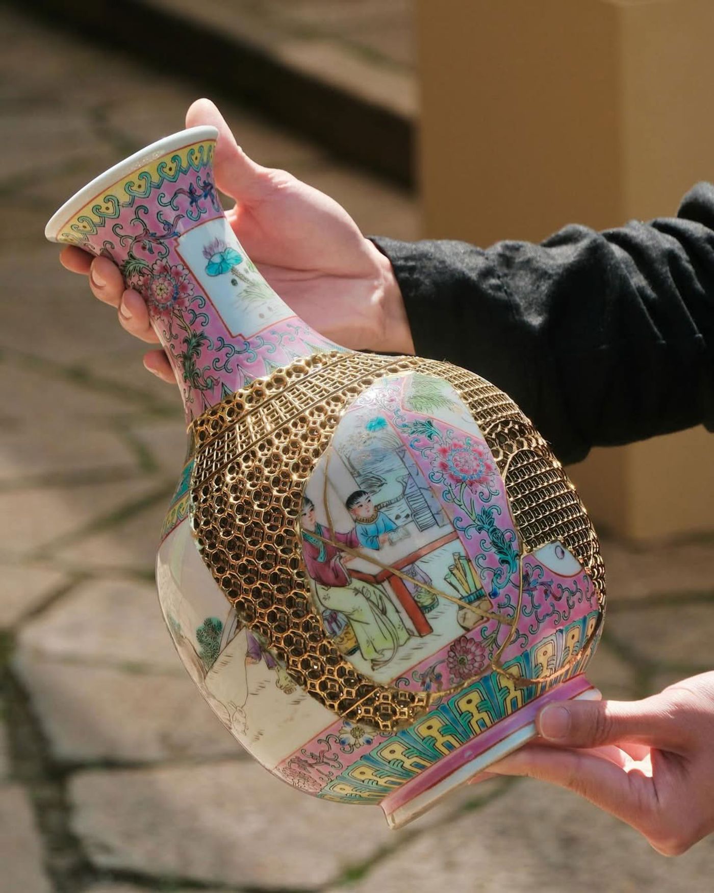 Hands presenting a restored traditional Chinese vase, its delicate broken areas replaced with intricate golden meshwork.