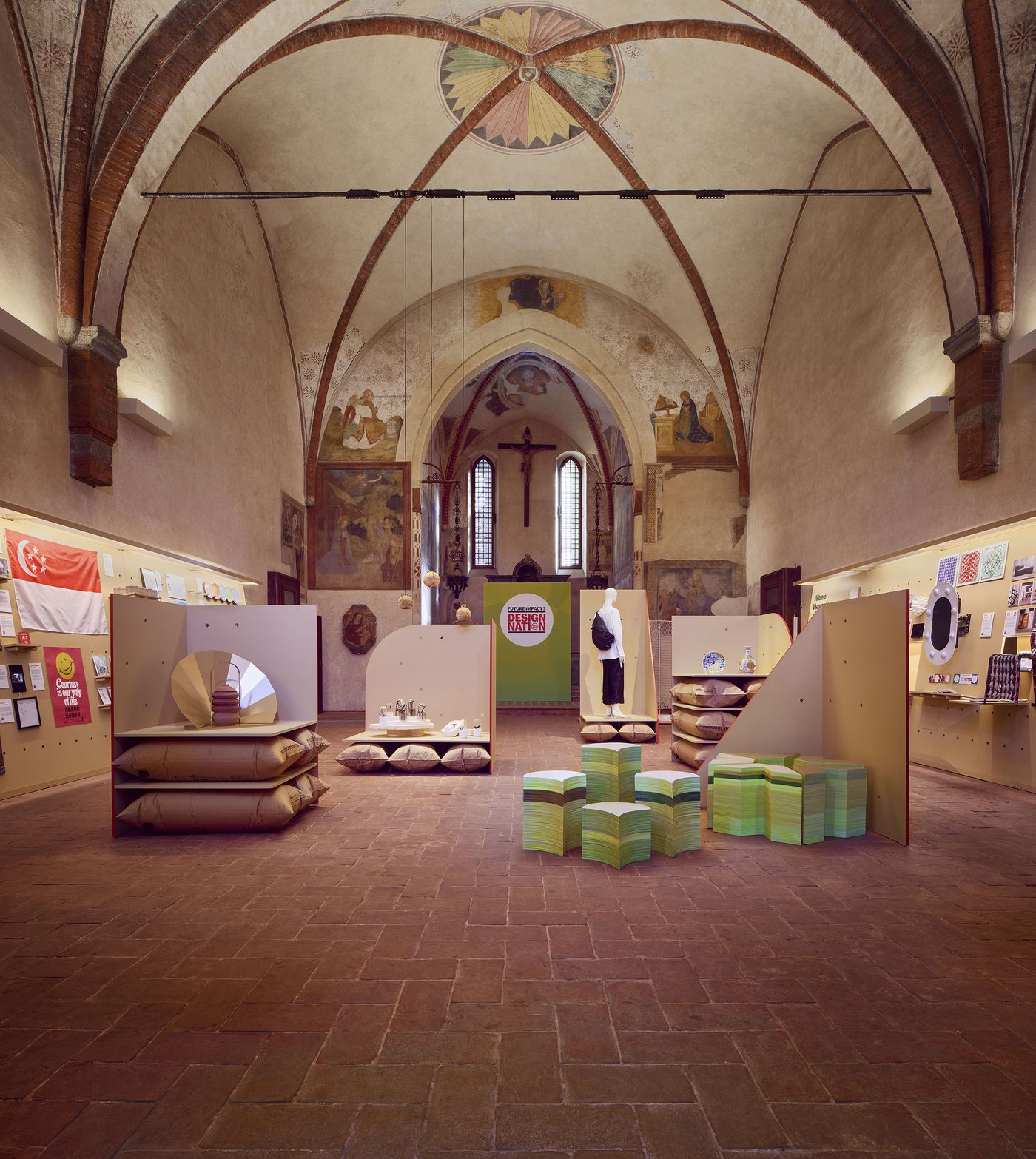 A grand exhibition space inside a historic church, showcasing design works including the golden-repaired plate and vase on a central mustard display.