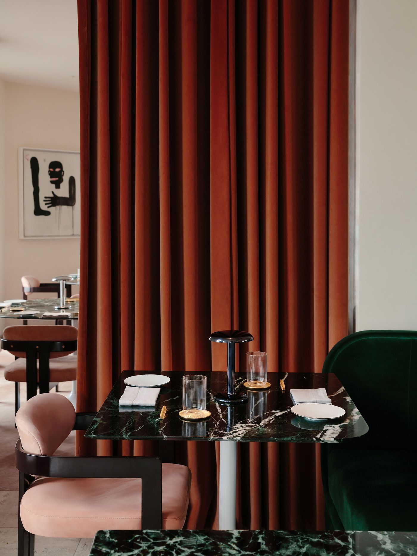 The glossy black Gustave lamp rests on a richly veined green marble table set for two, framed by velvet seating and terracotta curtains in a refined restaurant interior. The glossy black Gustave lamp rests on a richly veined green marble table set for two, framed by velvet seating and terracotta curtains in a refined restaurant interior.