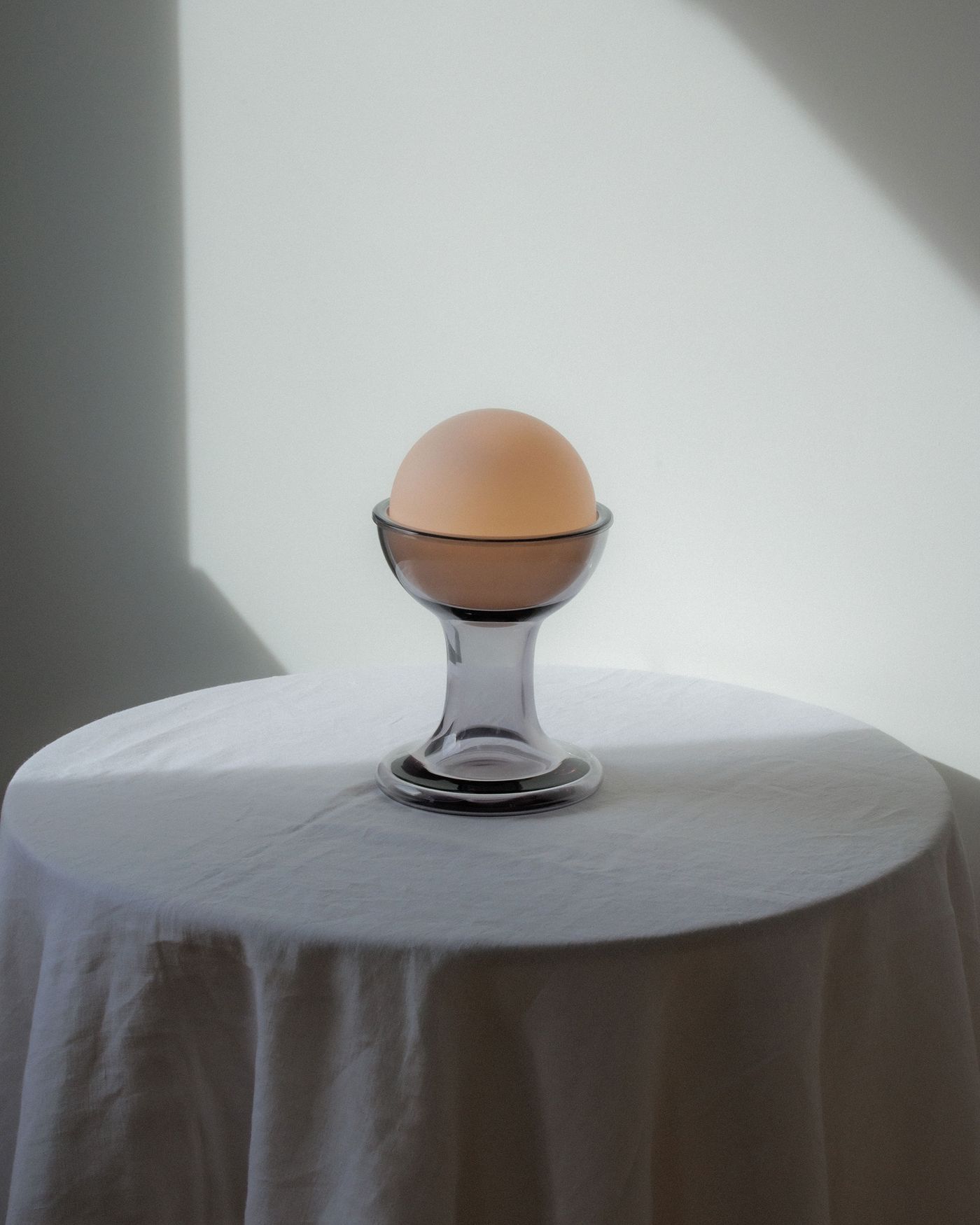 A clear glass Gelato table lamp with a pale orb diffuser, placed on a round white-clothed table, illuminated by directional natural light from the left. A clear glass Gelato table lamp with a pale orb diffuser, placed on a round white-clothed table, illuminated by directional natural light from the left.