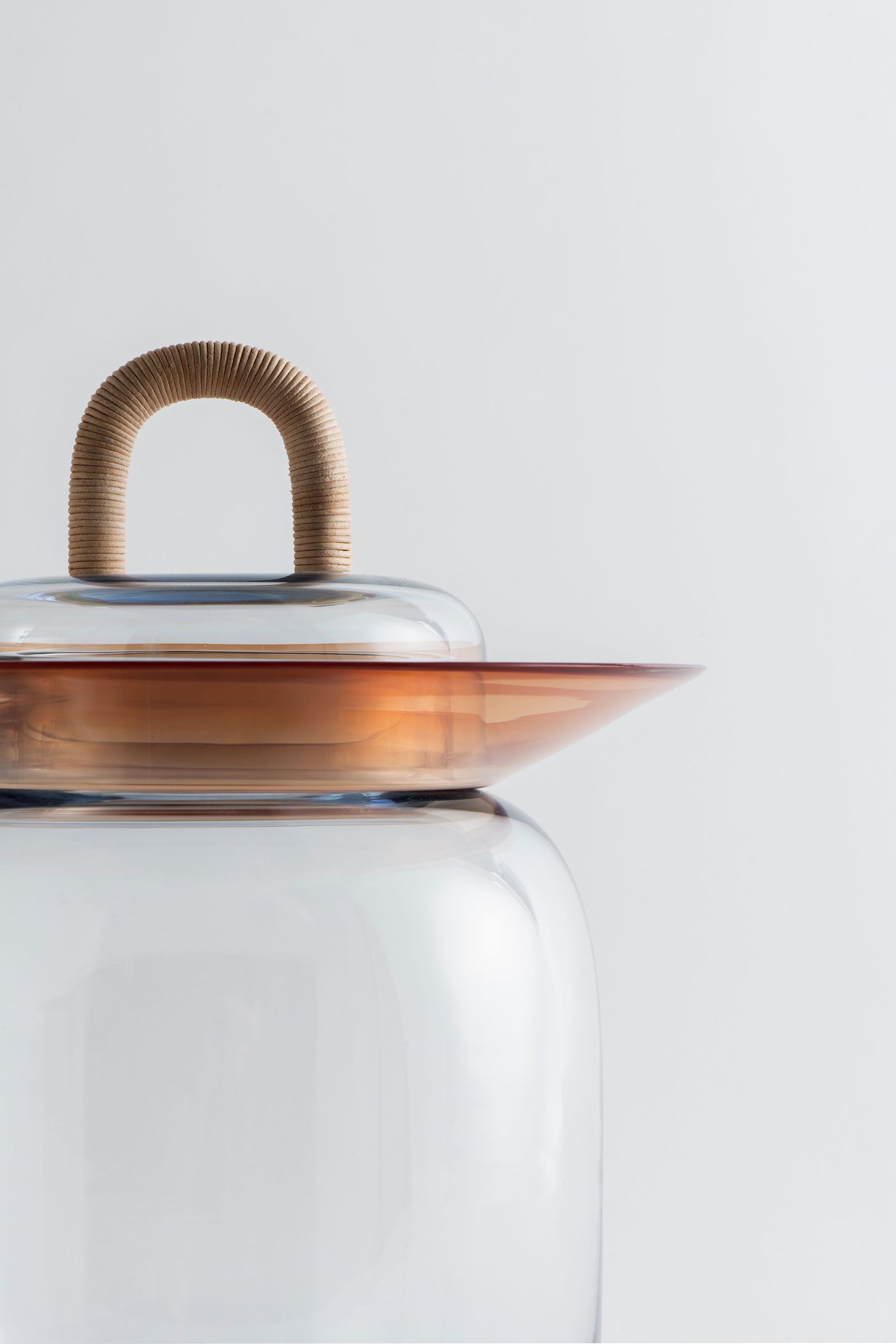 Close-up side view of the assembled glass vessel, highlighting the smooth curves of the clear jar and the warm amber glass rim.