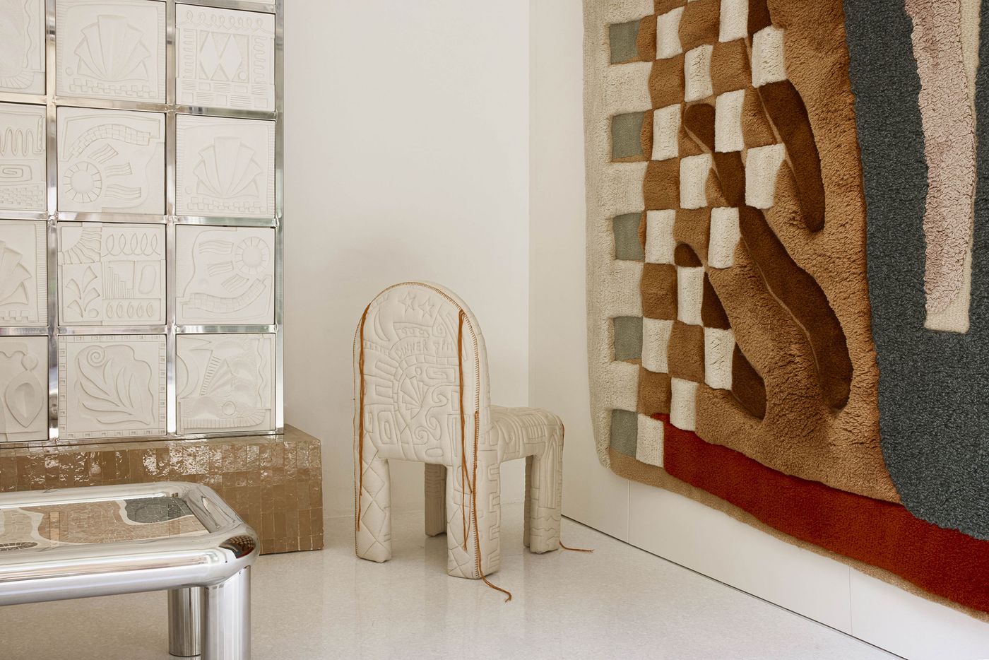 Minimalist corner with a sculptural cream chair, a patchwork wall tapestry, and a gridded installation of embossed tiles. Minimalist corner with a sculptural cream chair, a patchwork wall tapestry, and a gridded installation of embossed tiles.