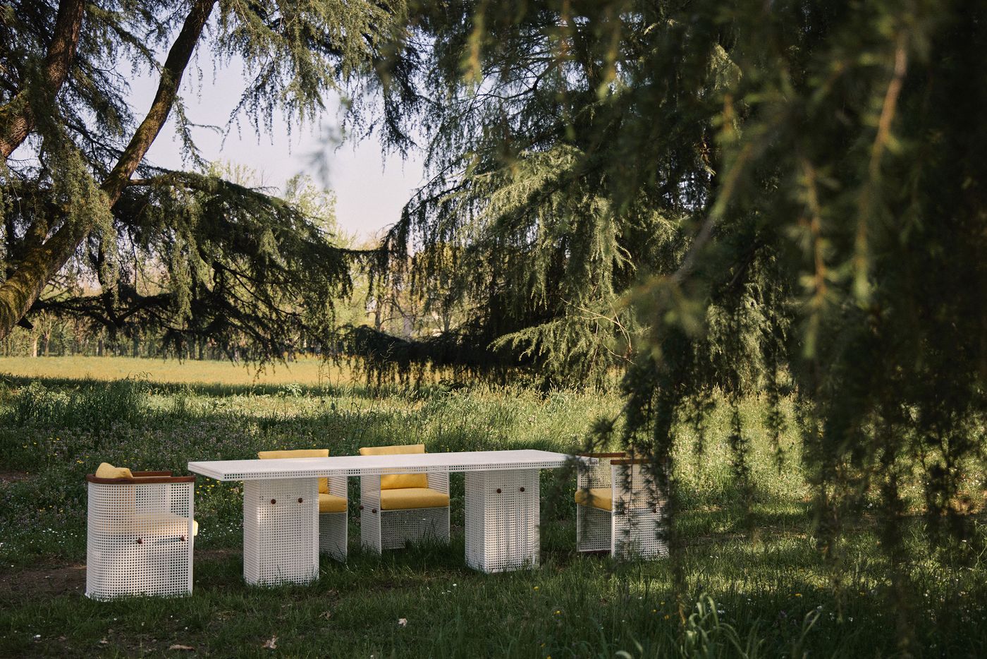 Outdoor dining set by Lemon with perforated white metal frames and yellow cushions, nestled under lush pine trees in a meadow at Villa Borsani during Milan Design Week 2025. Outdoor dining set by Lemon with perforated white metal frames and yellow cushions, nestled under lush pine trees in a meadow at Villa Borsani during Milan Design Week 2025.