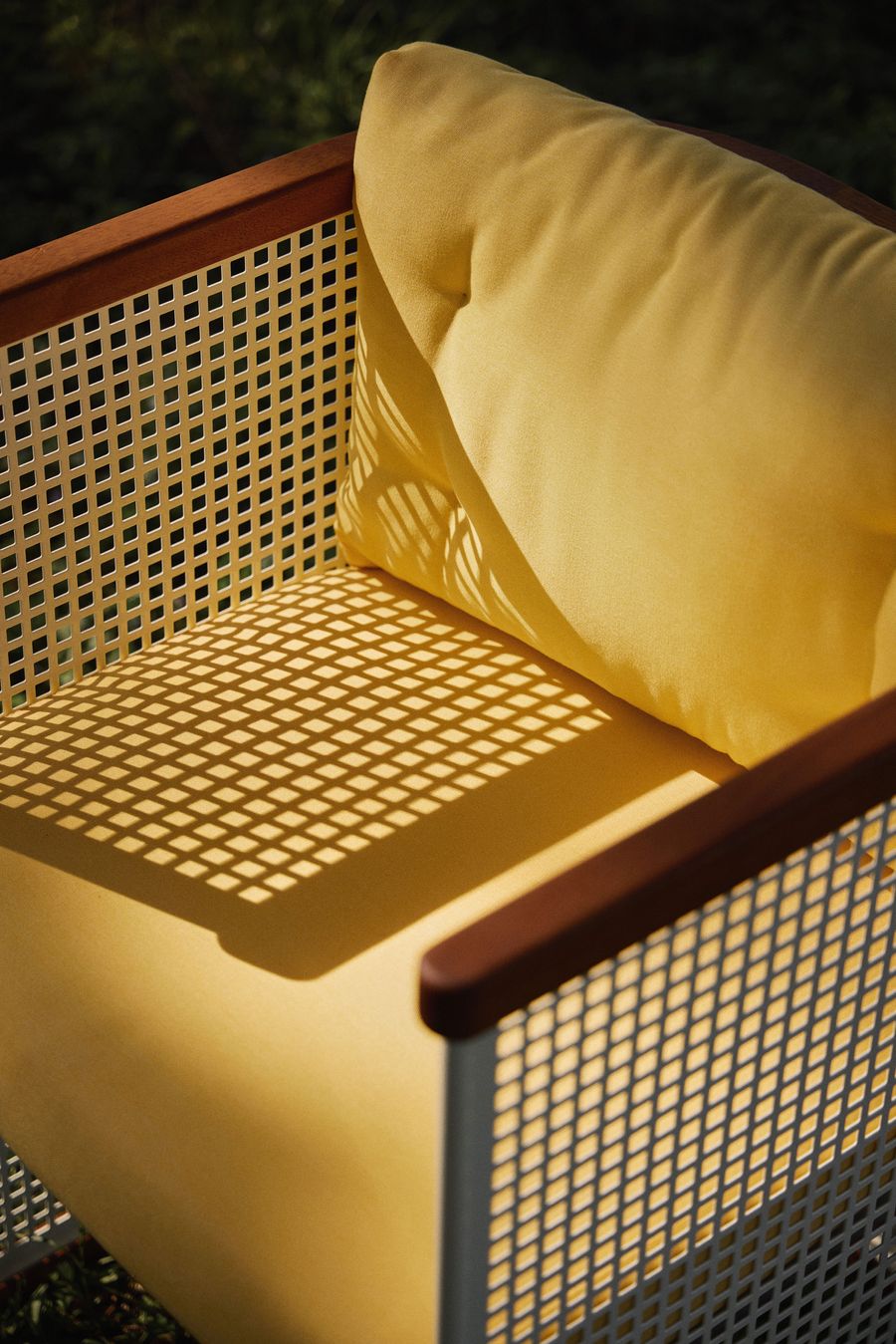 Close-up of a Lemon armchair showcasing the grid-like shadows cast on vibrant yellow upholstery through the white perforated frame. Close-up of a Lemon armchair showcasing the grid-like shadows cast on vibrant yellow upholstery through the white perforated frame.