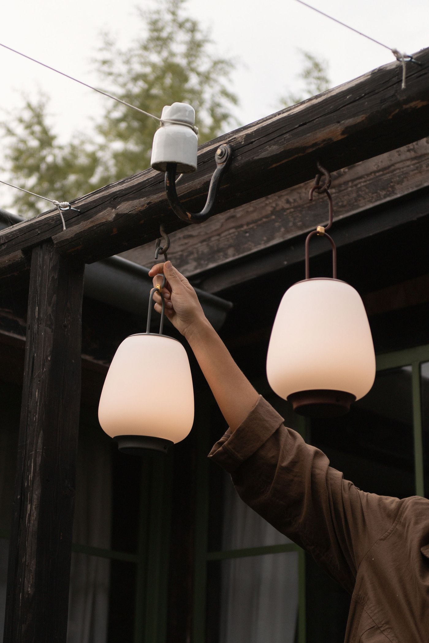 A soft matte lantern-style portable lamp being hooked onto a cable outdoors—evokes quiet evenings and functional beauty. A soft matte lantern-style portable lamp being hooked onto a cable outdoors—evokes quiet evenings and functional beauty.