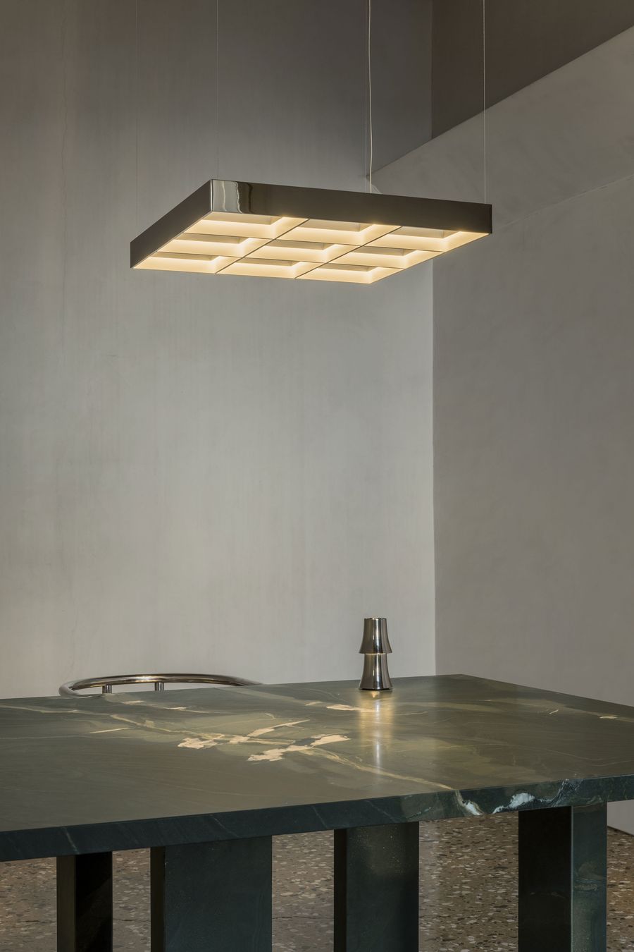 A sleek geometric pendant light floats above a deep green marble table, where minimalist design meets natural drama in perfect harmony. A sleek geometric pendant light floats above a deep green marble table, where minimalist design meets natural drama in perfect harmony.