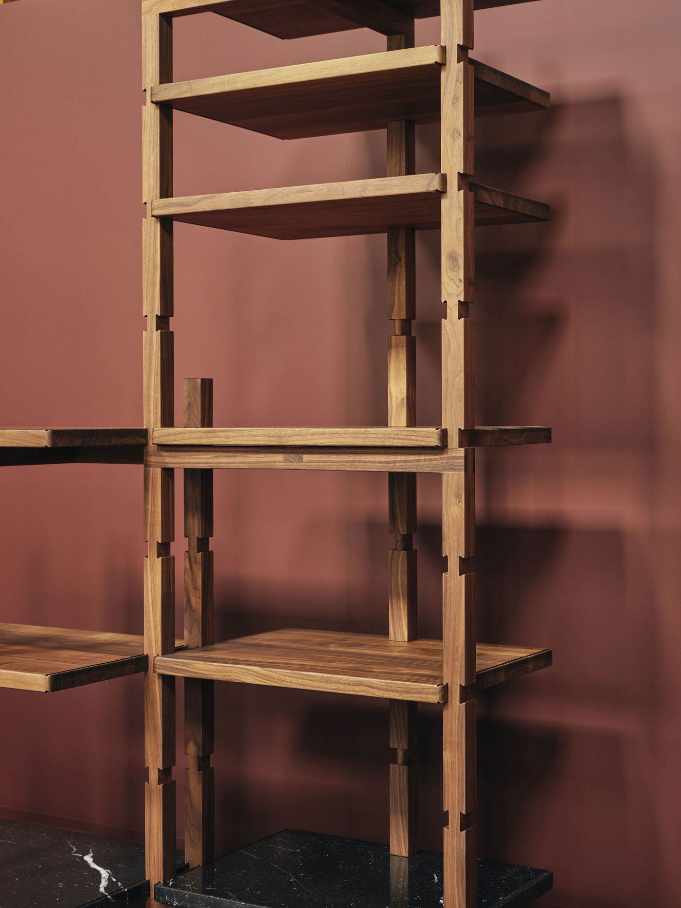 Close-up of a modular wooden shelving system, its clever joints and structure highlighted against a deep burgundy backdrop.