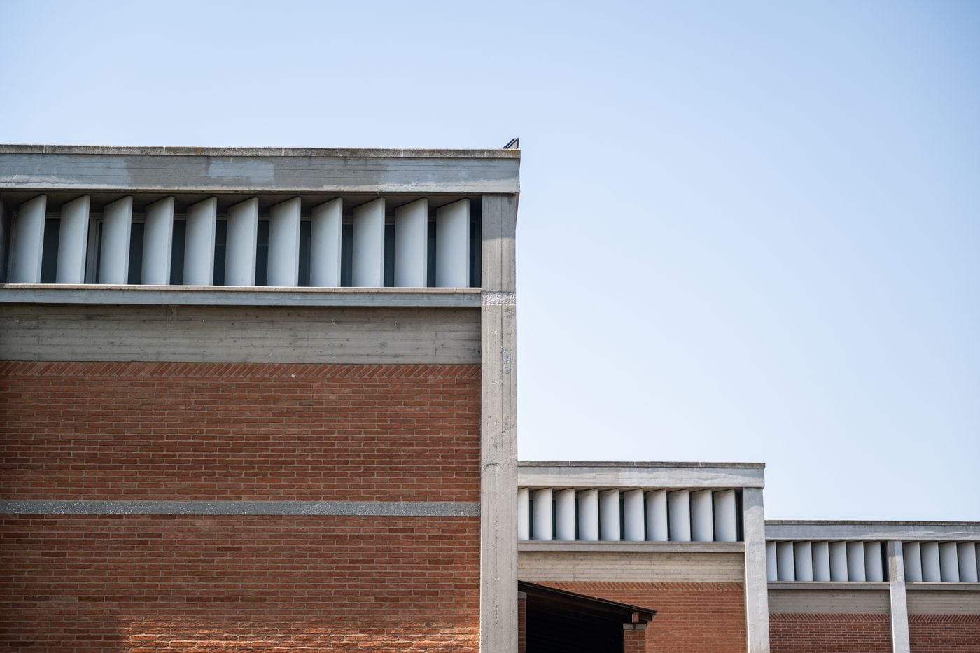 Architectural detail of the Museum of Byzantine Culture in Thessaloniki, highlighting its modernist composition of exposed concrete frames, red-brick walls and rhythmic vertical window fins. The stepped building volumes and restrained geometric detailing reflect the museum’s distinctive architectural language against a clear blue sky.