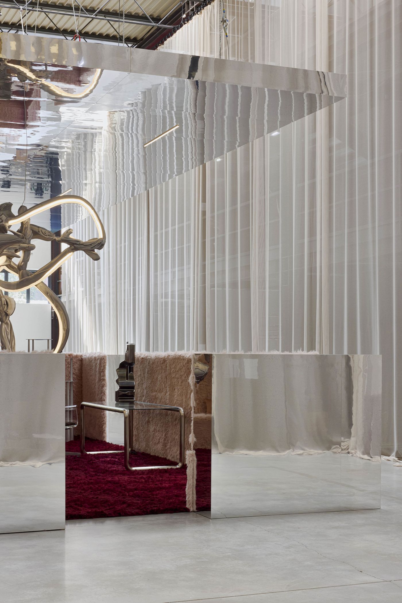 A mirrored canopy floats above fuzzy blush partitions and a plush burgundy carpet—surreal softness meets industrial reflection. A mirrored canopy floats above fuzzy blush partitions and a plush burgundy carpet—surreal softness meets industrial reflection.