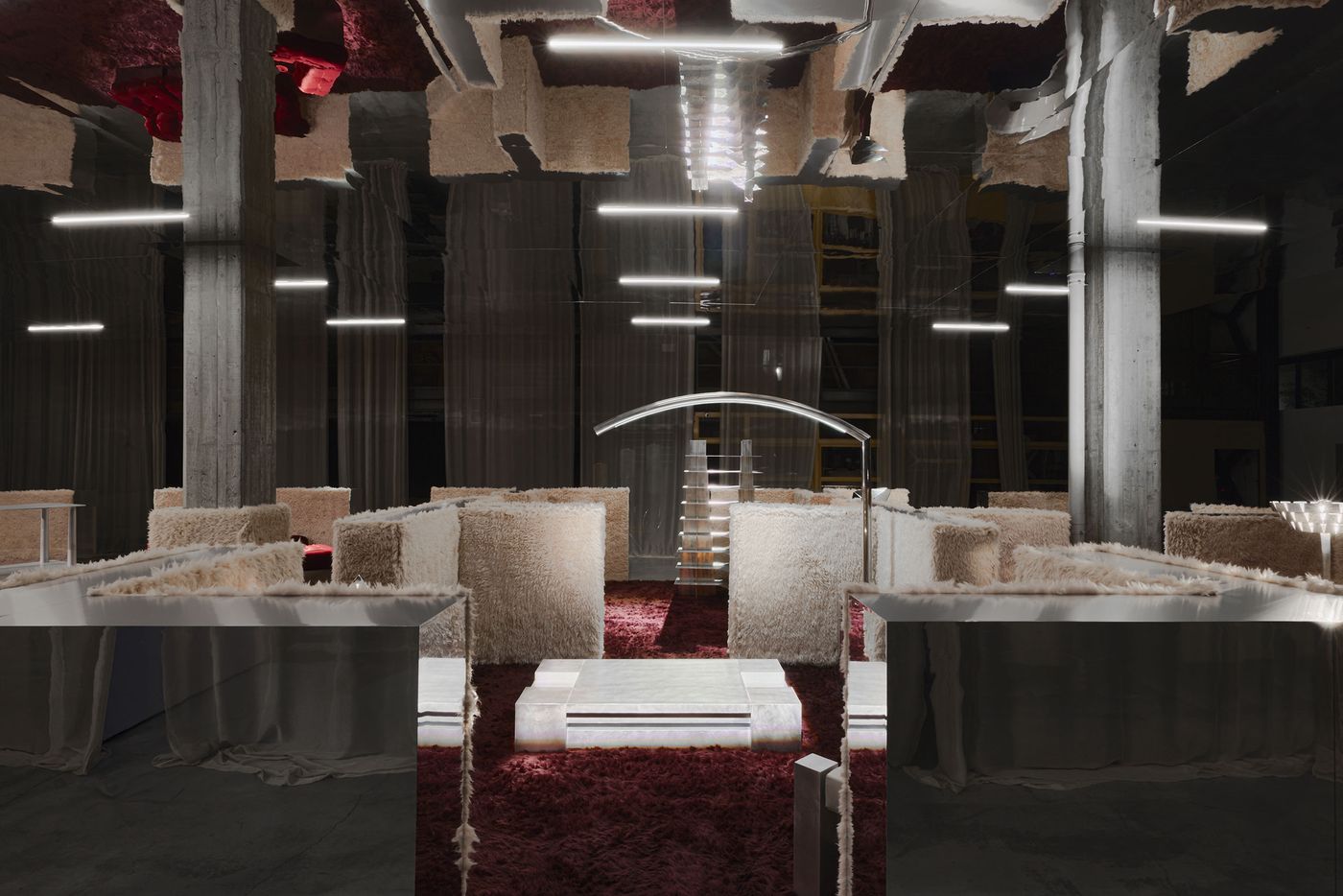 A maze of furry walls and mirrored surfaces glows under linear lights—like walking through a futuristic cocoon. A maze of furry walls and mirrored surfaces glows under linear lights—like walking through a futuristic cocoon.