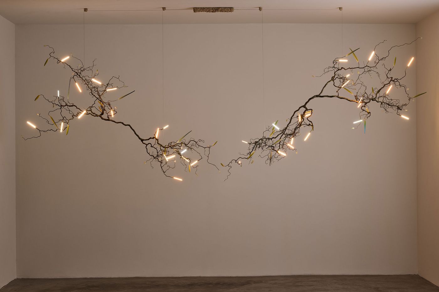 The same sculptural light piece in a dimly lit space, with its glowing rods activated—casting warm, organic light that highlights the twisting branches and scattered colored accents, evoking a floating, bioluminescent forest. The same sculptural light piece in a dimly lit space, with its glowing rods activated—casting warm, organic light that highlights the twisting branches and scattered colored accents, evoking a floating, bioluminescent forest.