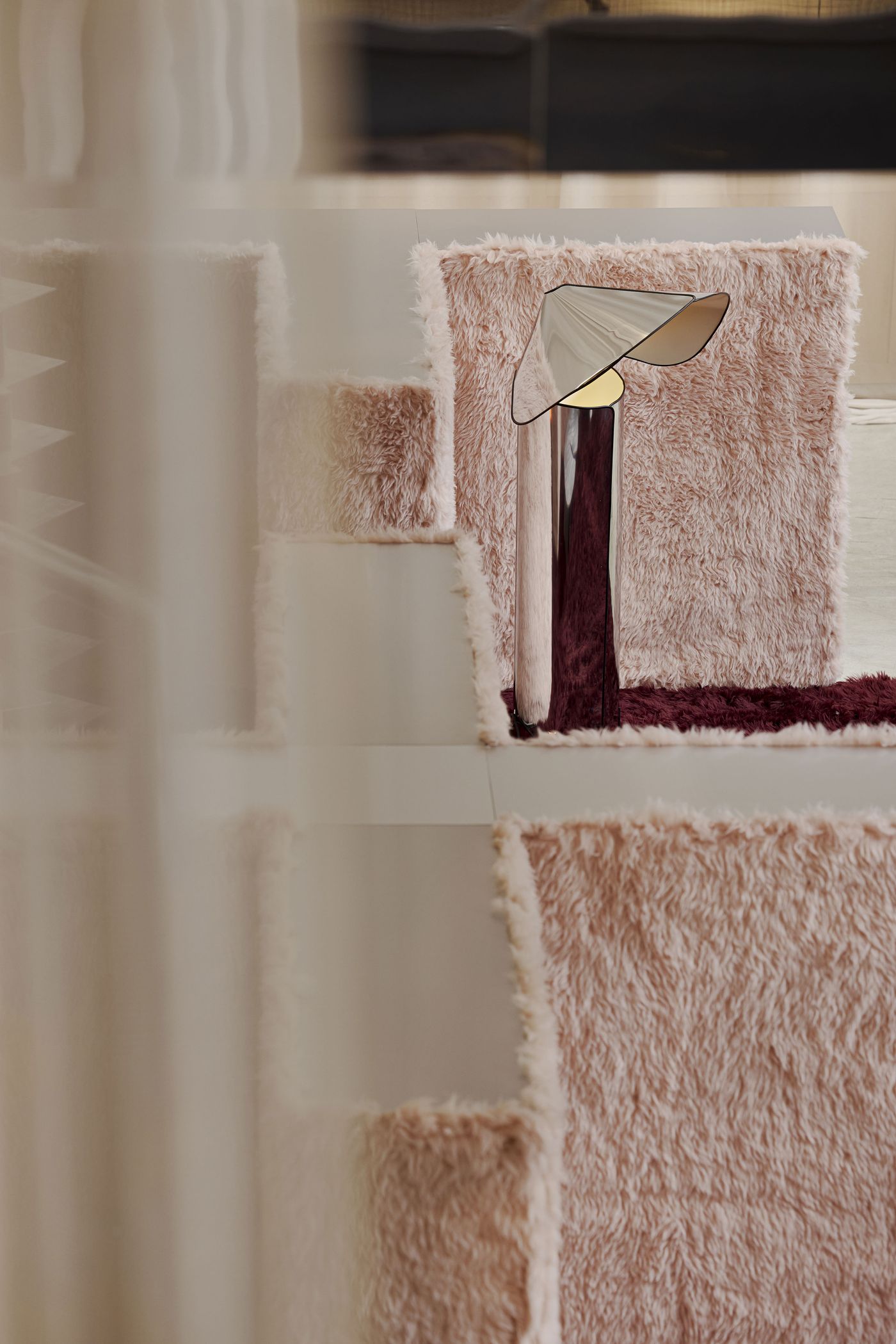 A polished lamp peeks through soft pink walls—couture coziness with a metallic wink.