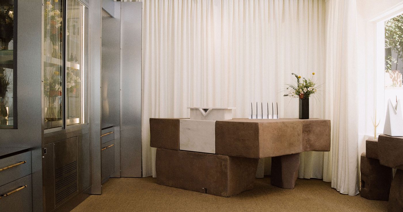 The minimalist interior of Phāon, a floral studio, perfumery and design store in Athens, features a sculptural counter assembled from chunky, earth-toned blocks, set against softly pleated ivory curtains. Metallic cabinetry, slender black display objects and an asymmetrical floral arrangement create a carefully composed dialogue between industrial materials, organic textures and contemporary design.