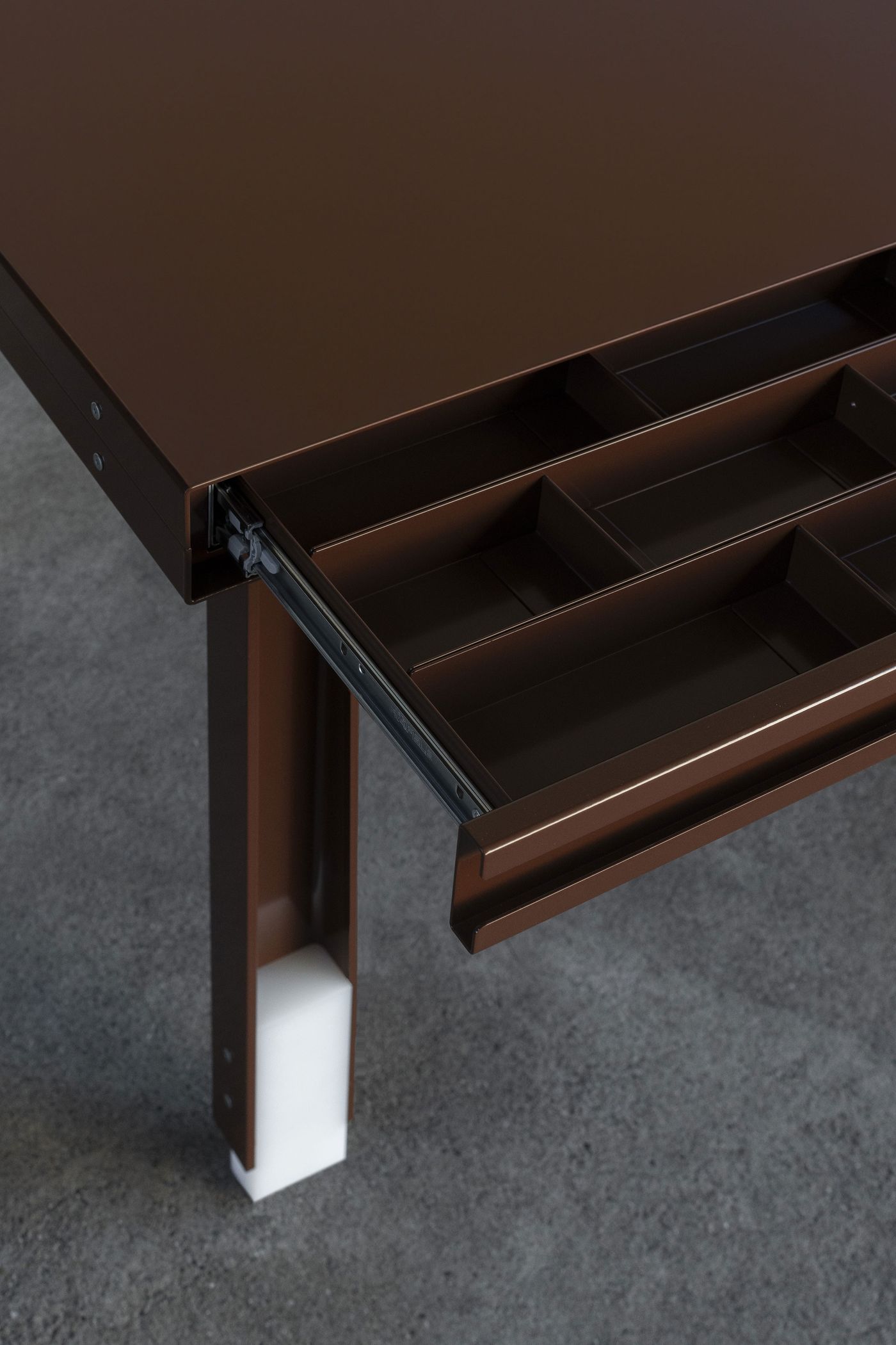 Close-up of a brown powder-coated metal table featuring an open drawer with neatly divided compartments—industrial detail rendered with quiet elegance. Close-up of a brown powder-coated metal table featuring an open drawer with neatly divided compartments—industrial detail rendered with quiet elegance.