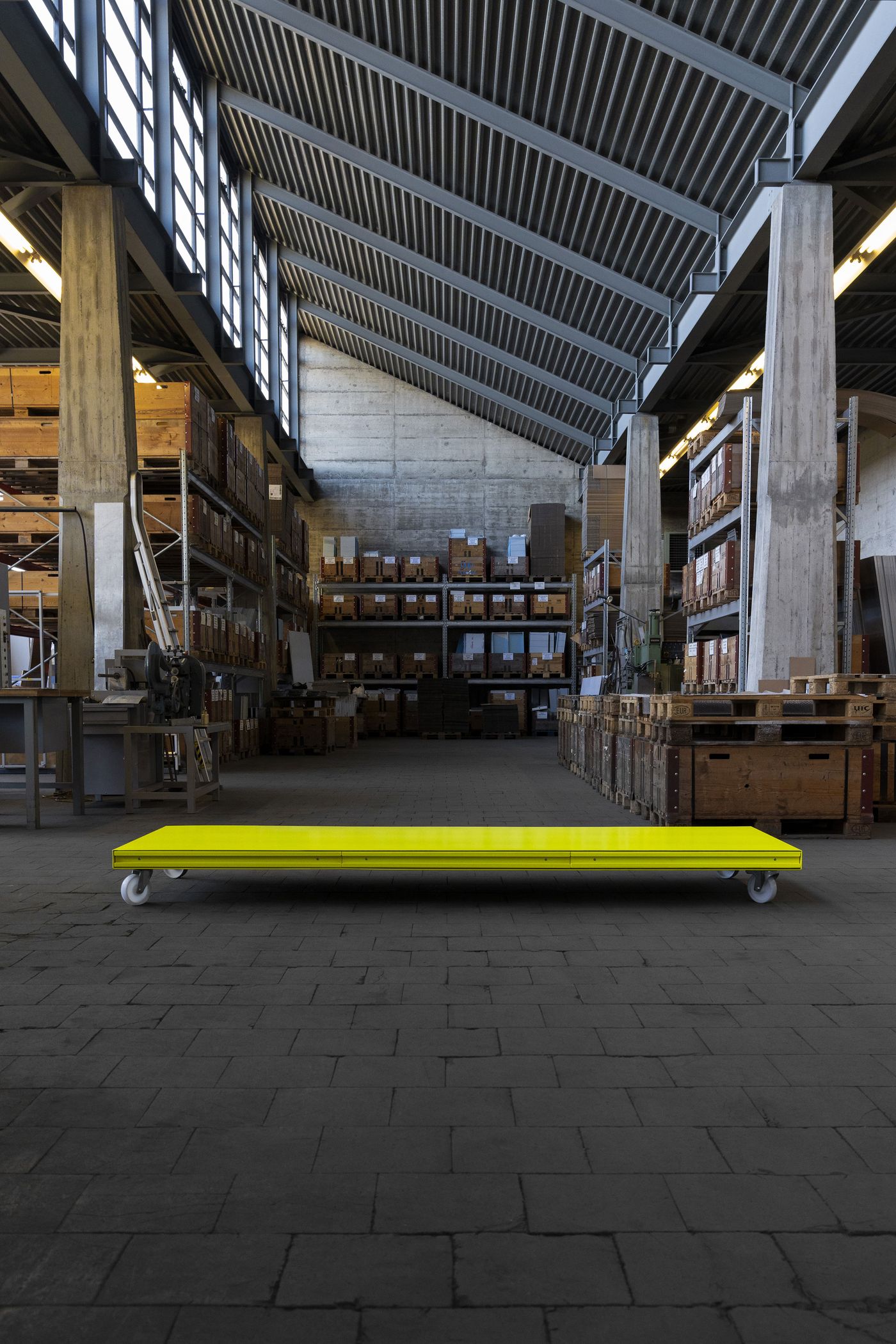 A vibrant yellow low-profile platform with wheels sits at the center of a vast industrial warehouse, its glossy surface glowing against the muted grey of concrete floors and exposed storage racks—design as punctuation in an architectural space. A vibrant yellow low-profile platform with wheels sits at the center of a vast industrial warehouse, its glossy surface glowing against the muted grey of concrete floors and exposed storage racks—design as punctuation in an architectural space.