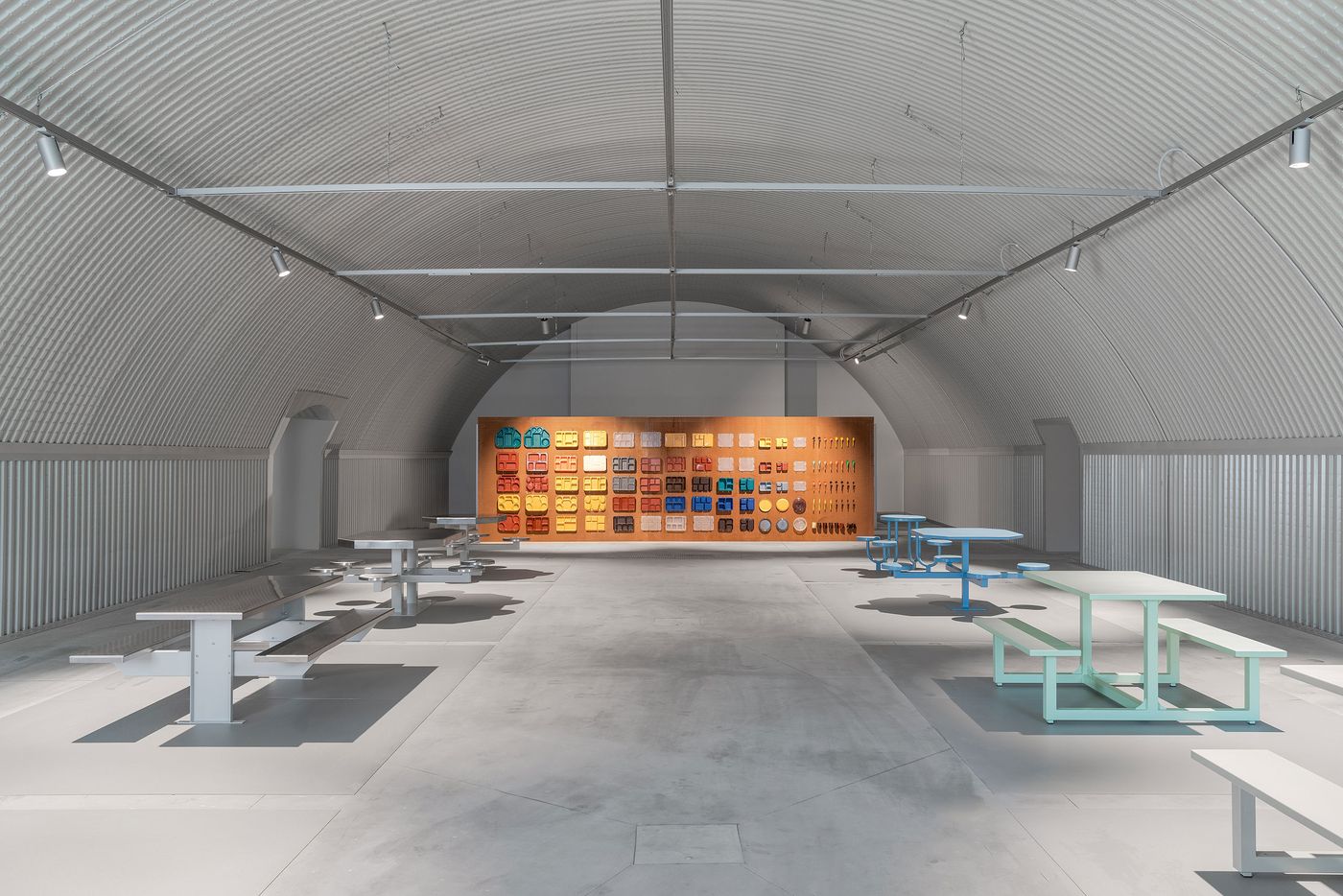 A lineup of colorful prison phone booths and metal security doors displayed like sculptures in a gallery space. A lineup of colorful prison phone booths and metal security doors displayed like sculptures in a gallery space.