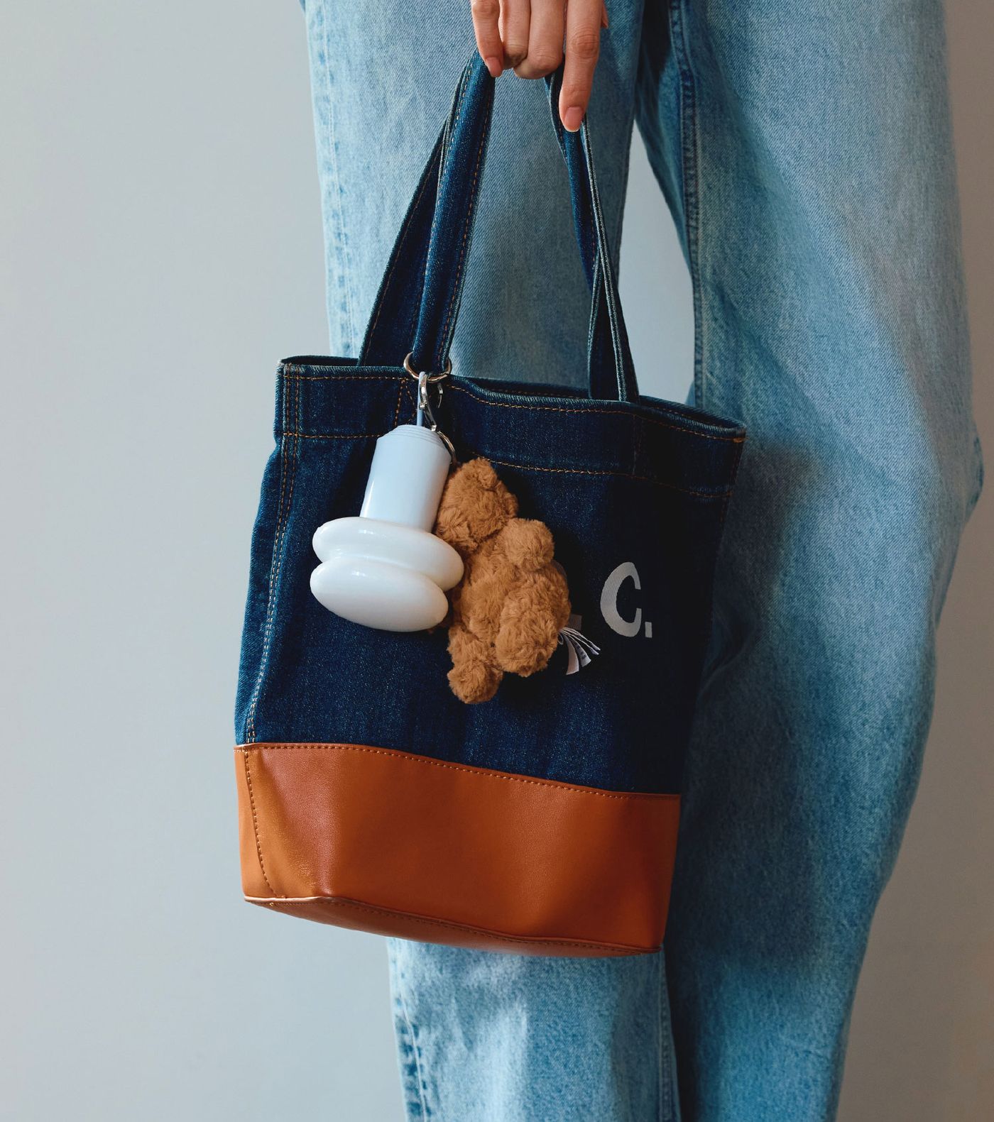 A white mini Snowman8 lamp clipped onto a denim tote bag with tan leather base, next to a teddy bear keychain — the perfect portable glow-on-the-go.