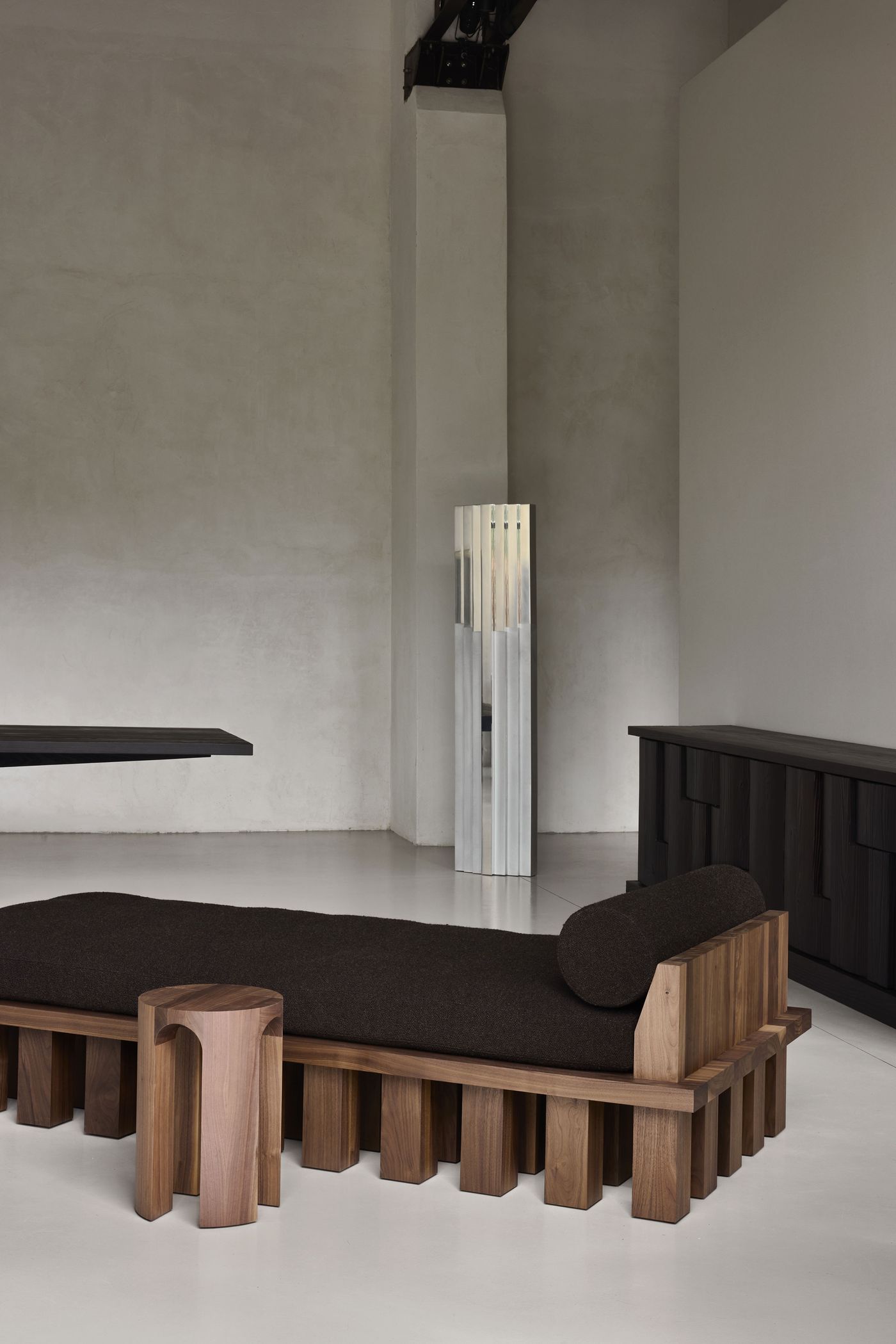 sculptural wooden daybed with a dark cushion and matching side table in a minimal, industrial space. sculptural wooden daybed with a dark cushion and matching side table in a minimal, industrial space.